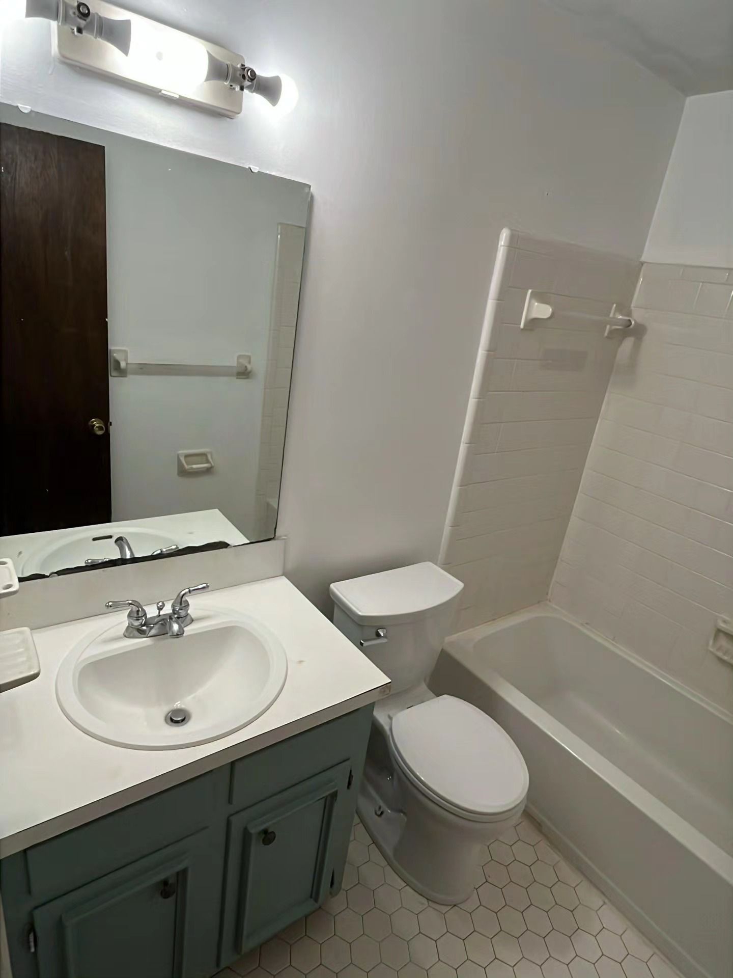 Small bathroom with sink, toilet, bathtub, mirror, and green vanity cabinets