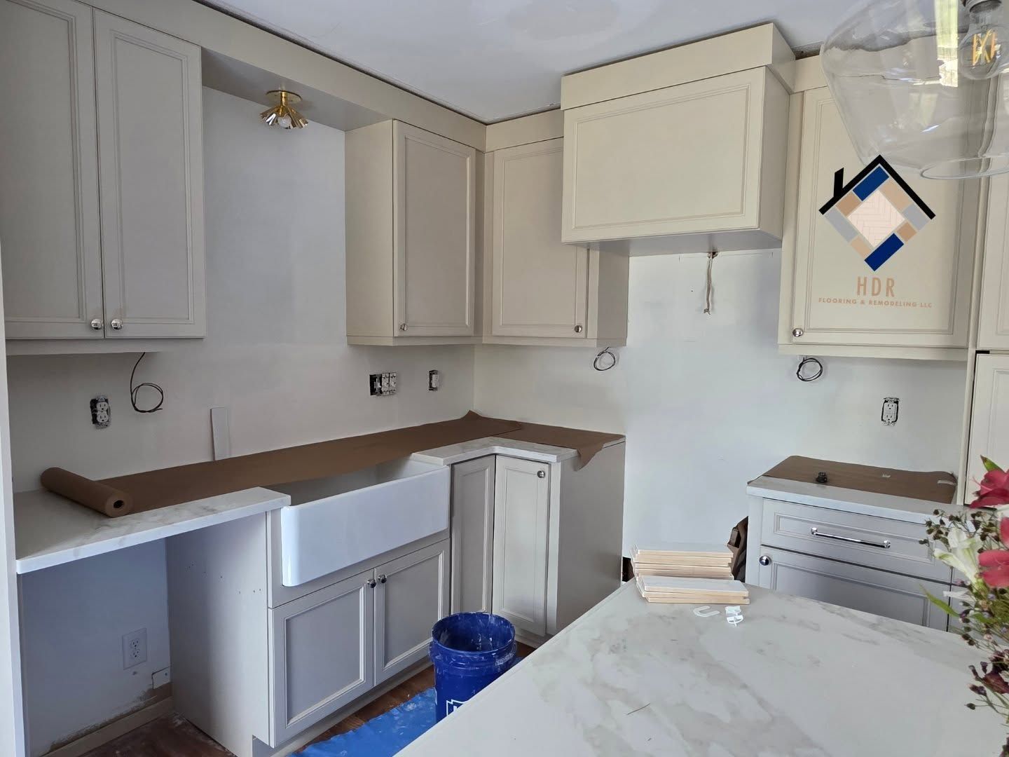 Small white kitchen under renovation with unfinished cabinets, countertops, and a blue bucket on the floor