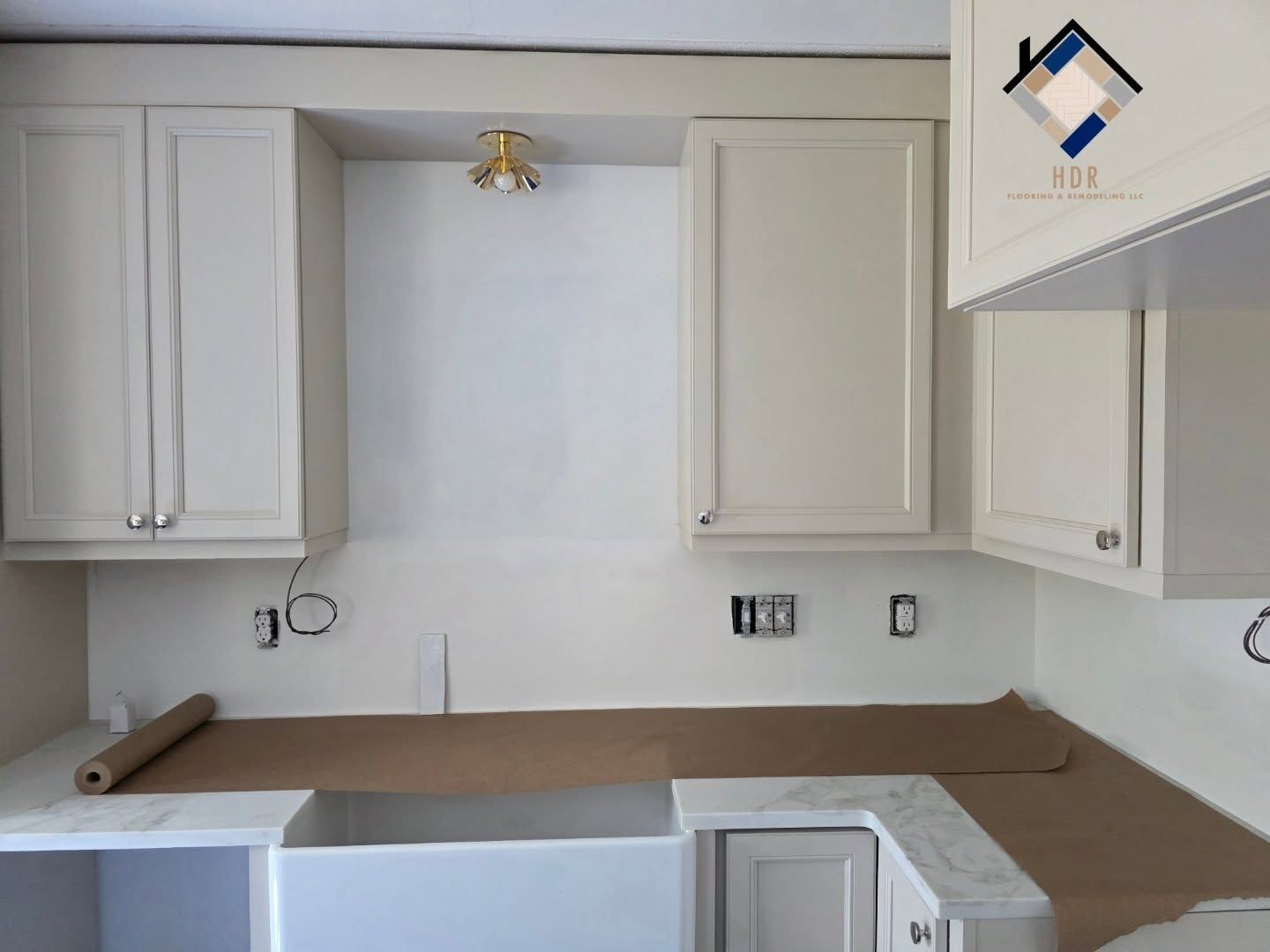 Unfinished kitchen with white cabinets, beige countertops, and sink cutouts along a wall
