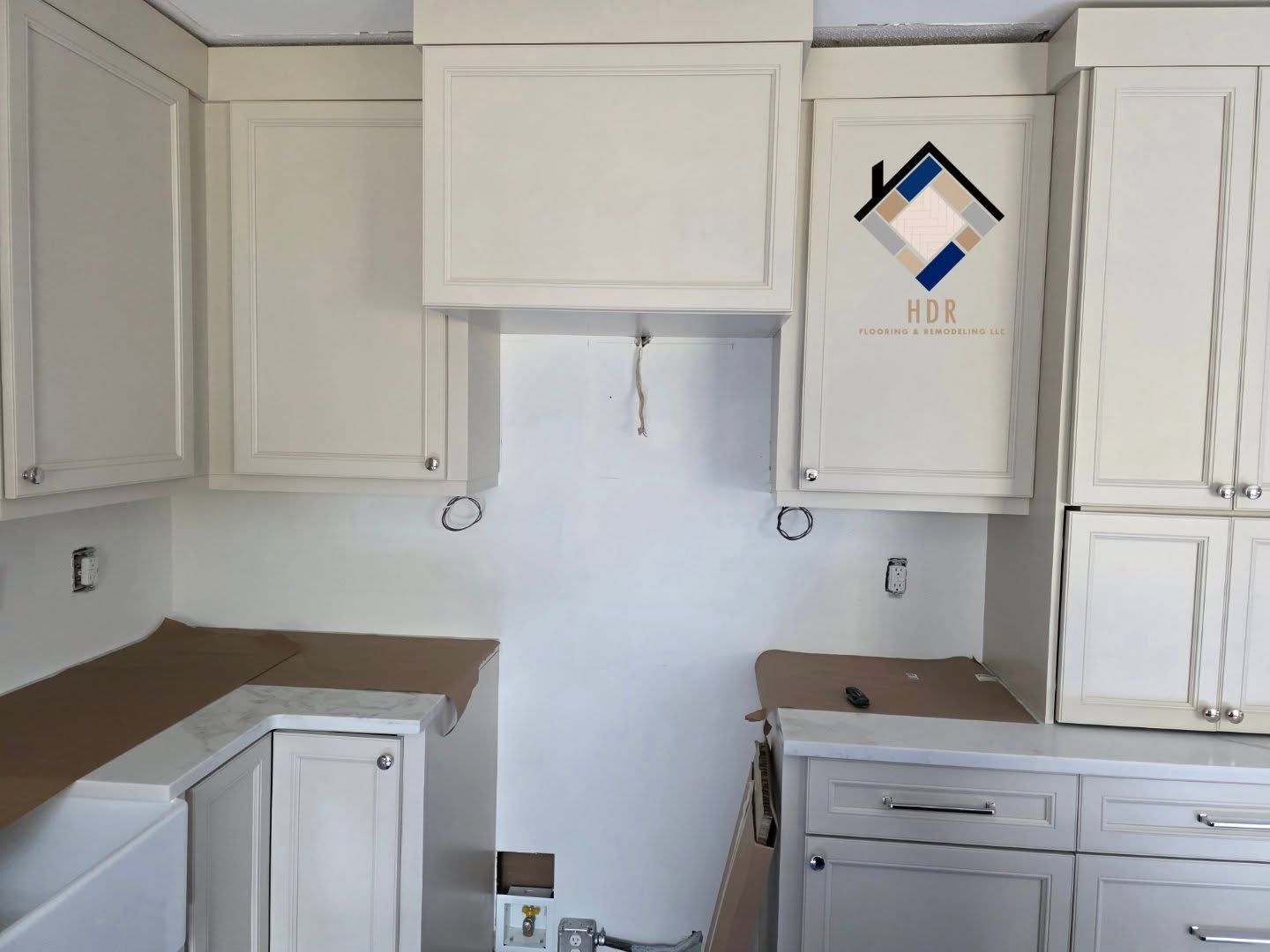 Empty kitchen under renovation with white cabinets, gray countertops, and unfinished wall outlets