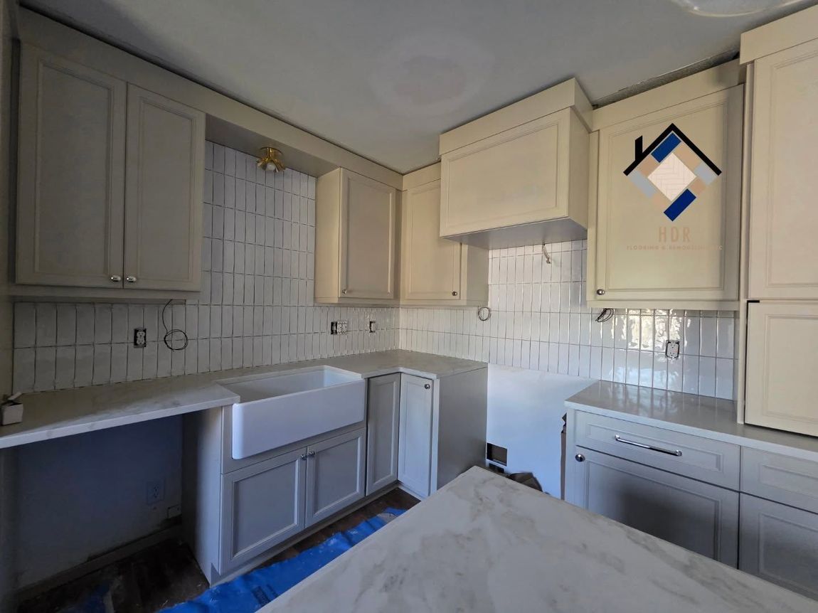 Small beige kitchen with white cabinets, tiled backsplash, sink, and countertop under construction.
