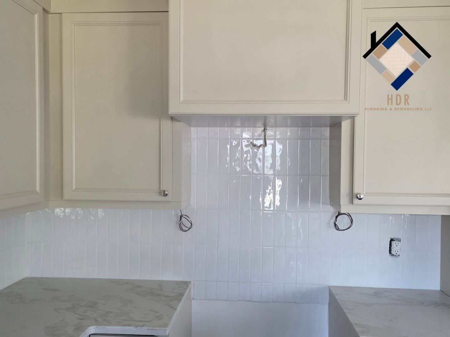 Empty kitchen with white cabinets, glossy white tile backsplash, and a gray countertop.