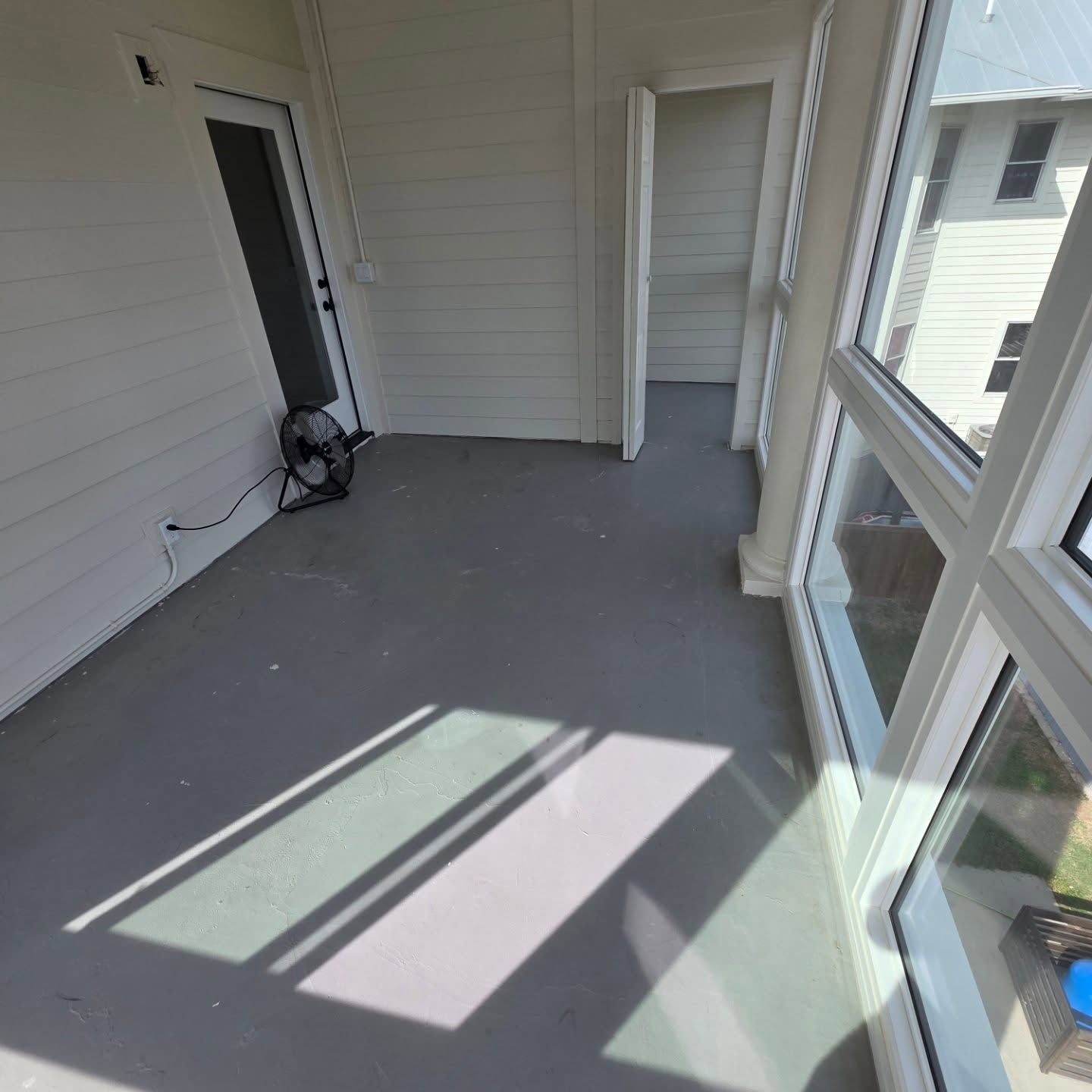 Empty screened porch with gray floor, white walls, and sunlight streaming through windows.