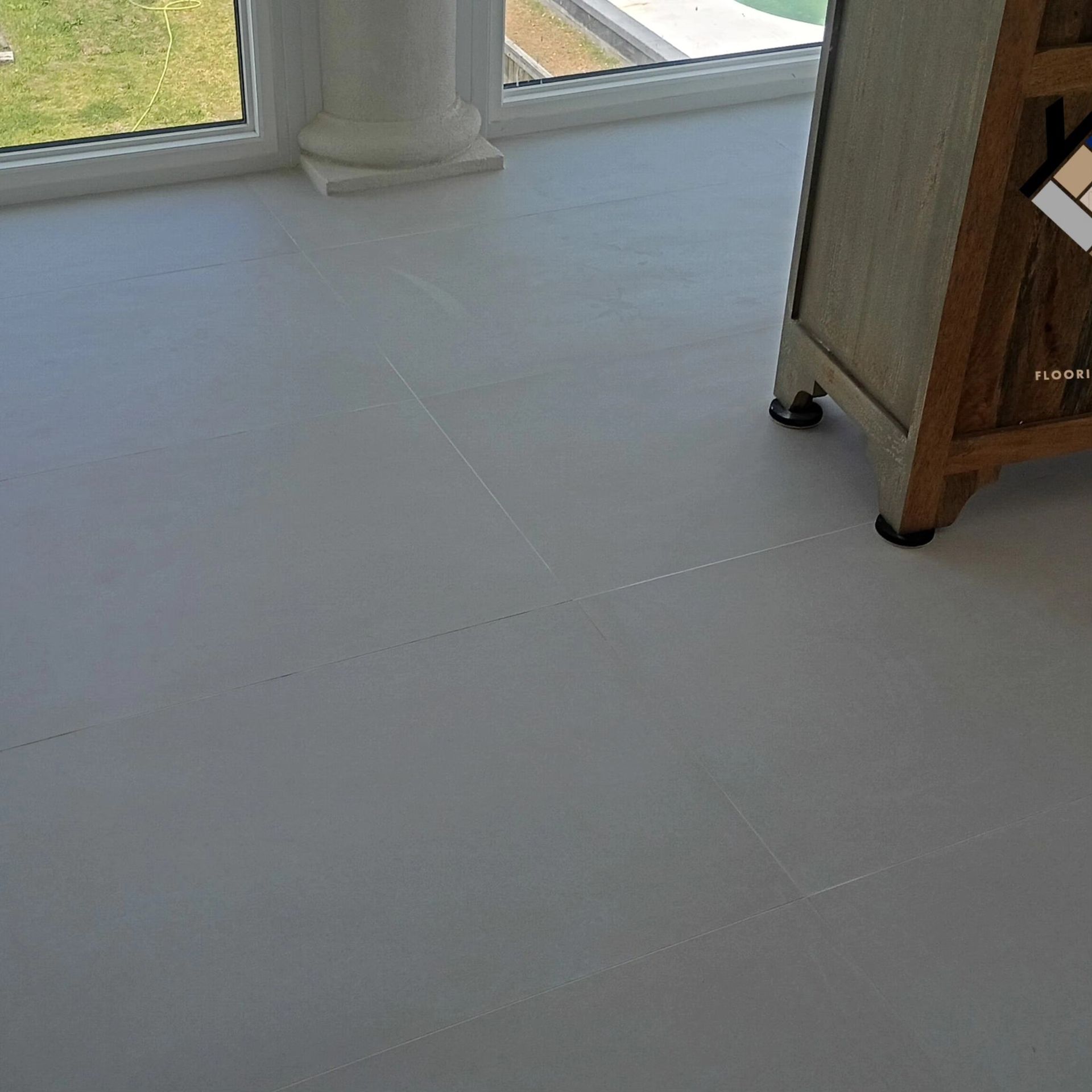 Empty light-gray tiled floor beside windows and a wooden cabinet in a bright room