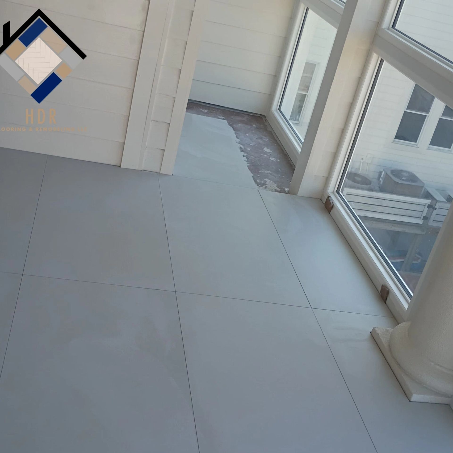Bright tiled hallway with windows, white walls, and a column, leading to a doorway.
