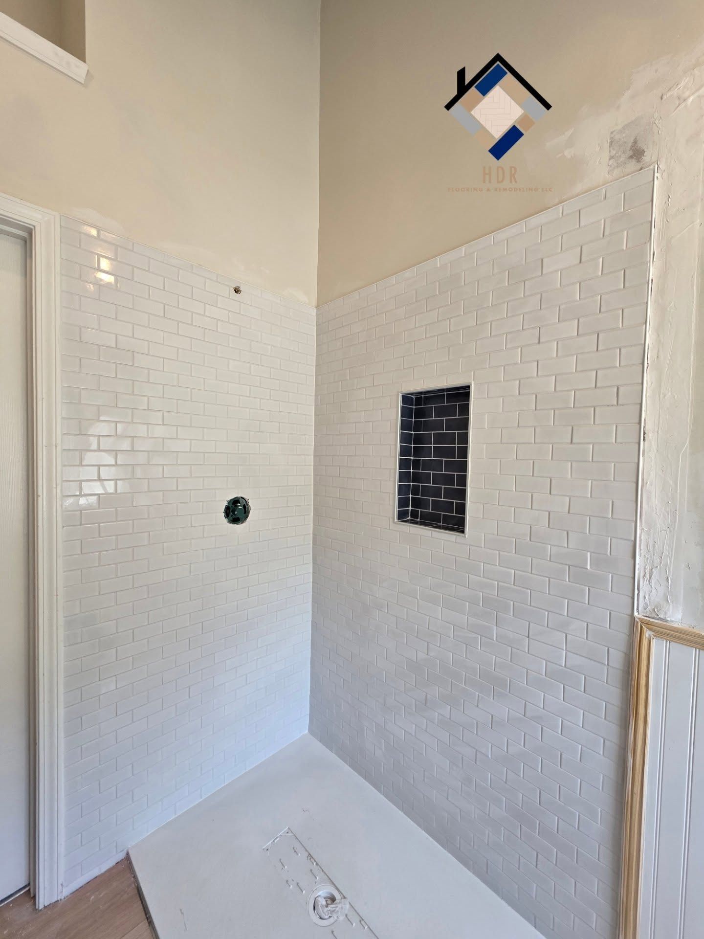 White-tiled shower with built-in niche and open glass door in a bathroom￼