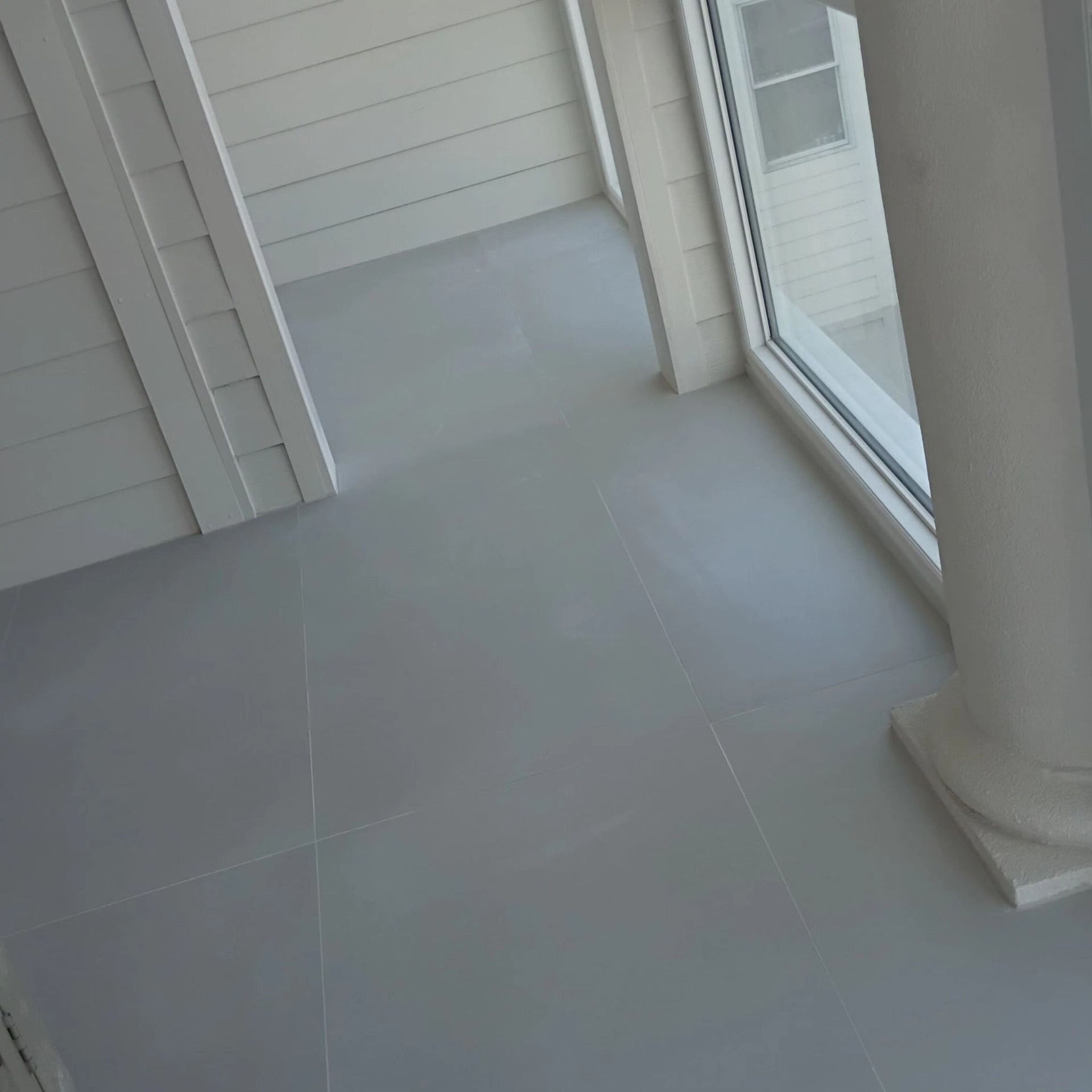 Empty tiled porch with white siding, sliding glass door, and a column.