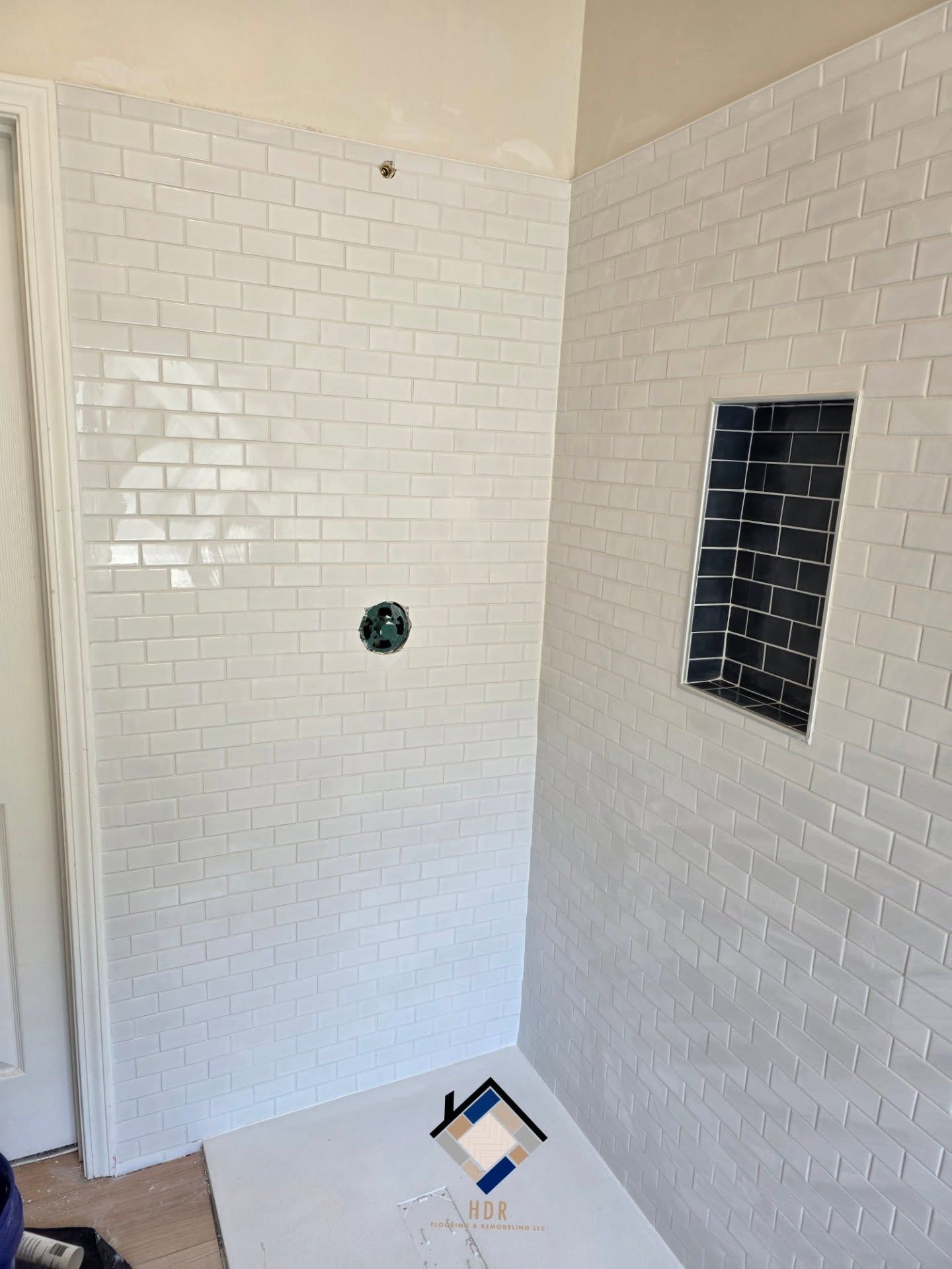 White-tiled shower stall with a shower valve and a recessed wall niche, viewed from the doorway.