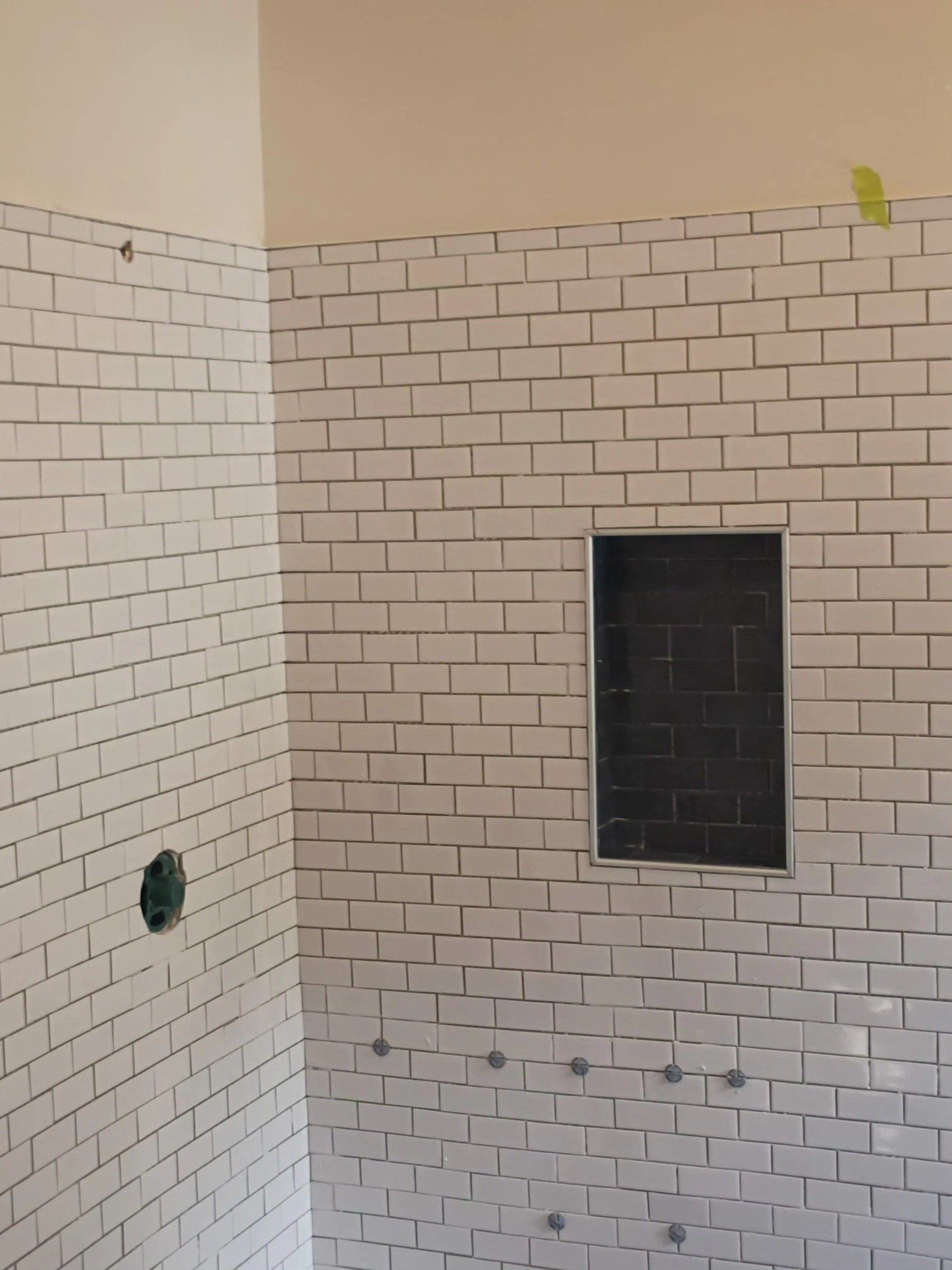 White tiled shower walls with a small black window opening.