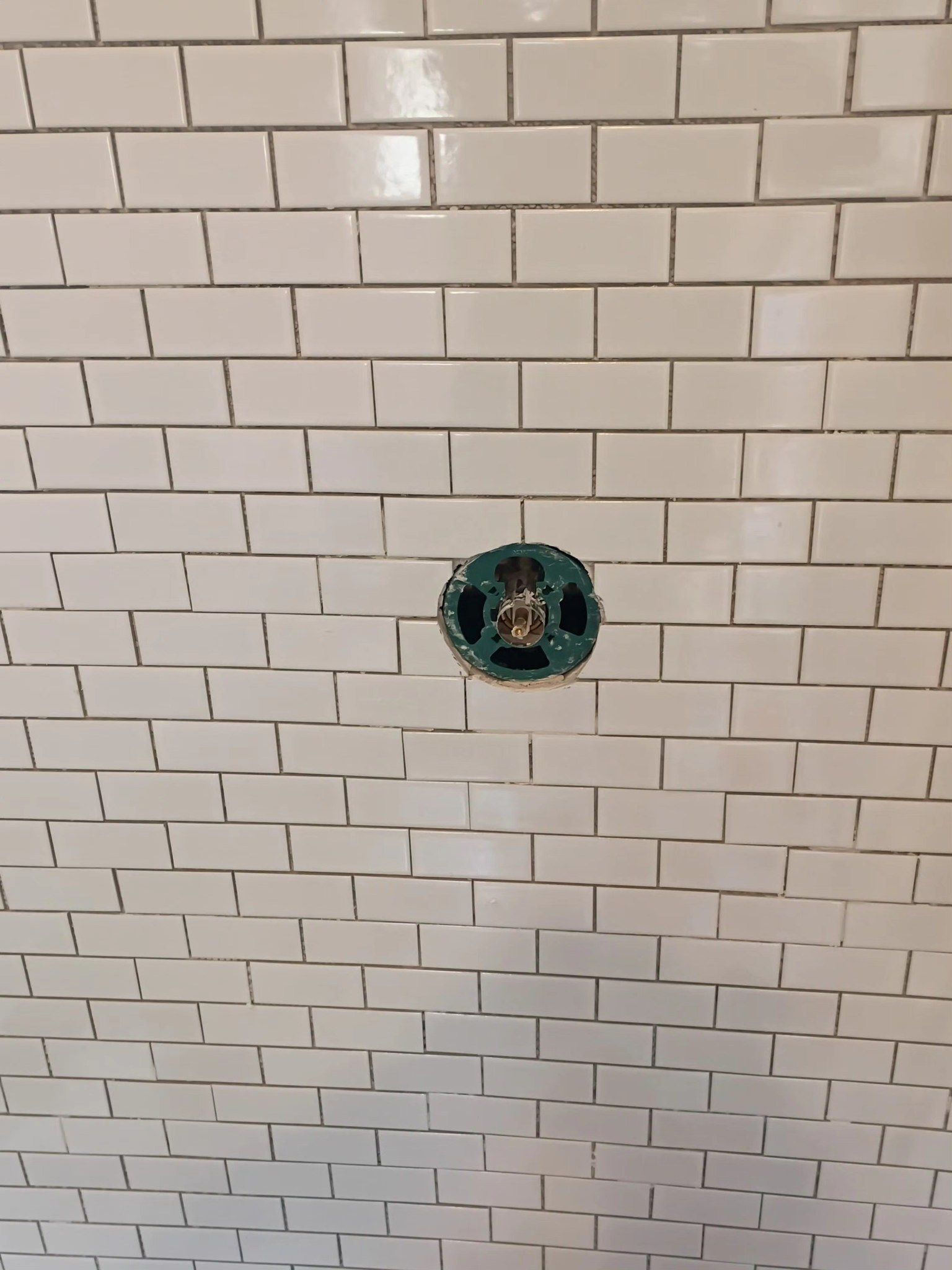 White tiled wall with a green electrical outlet opening at the center.