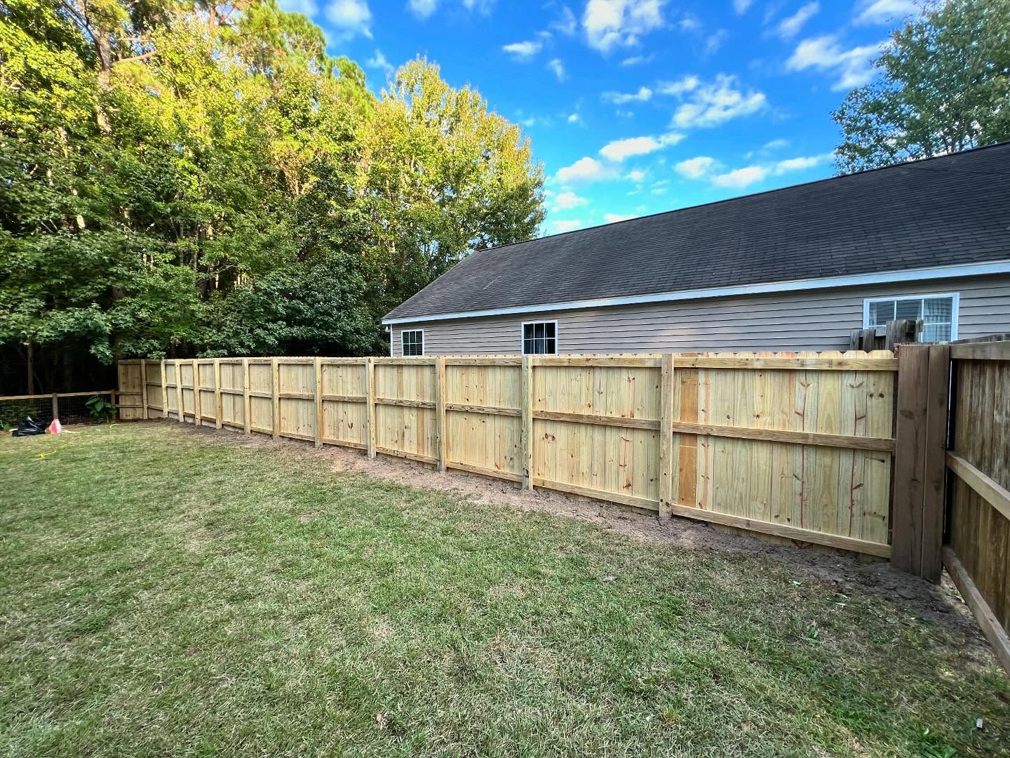Wooden privacy fence along a grassy backyard beside a house under a blue sky