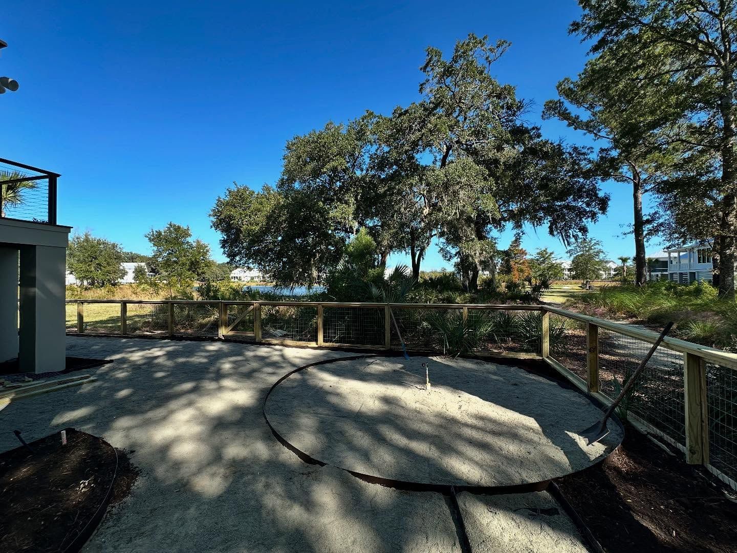 Circular concrete pad in a fenced park area with trees under a bright blue sky.