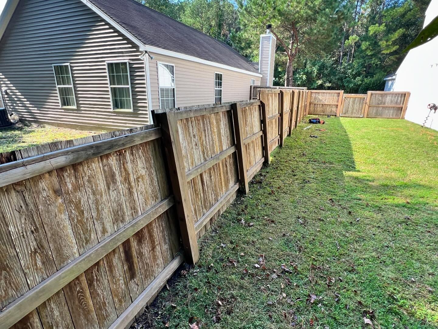 Weathered wooden fence along a grassy side yard beside a house, leading toward a patio.