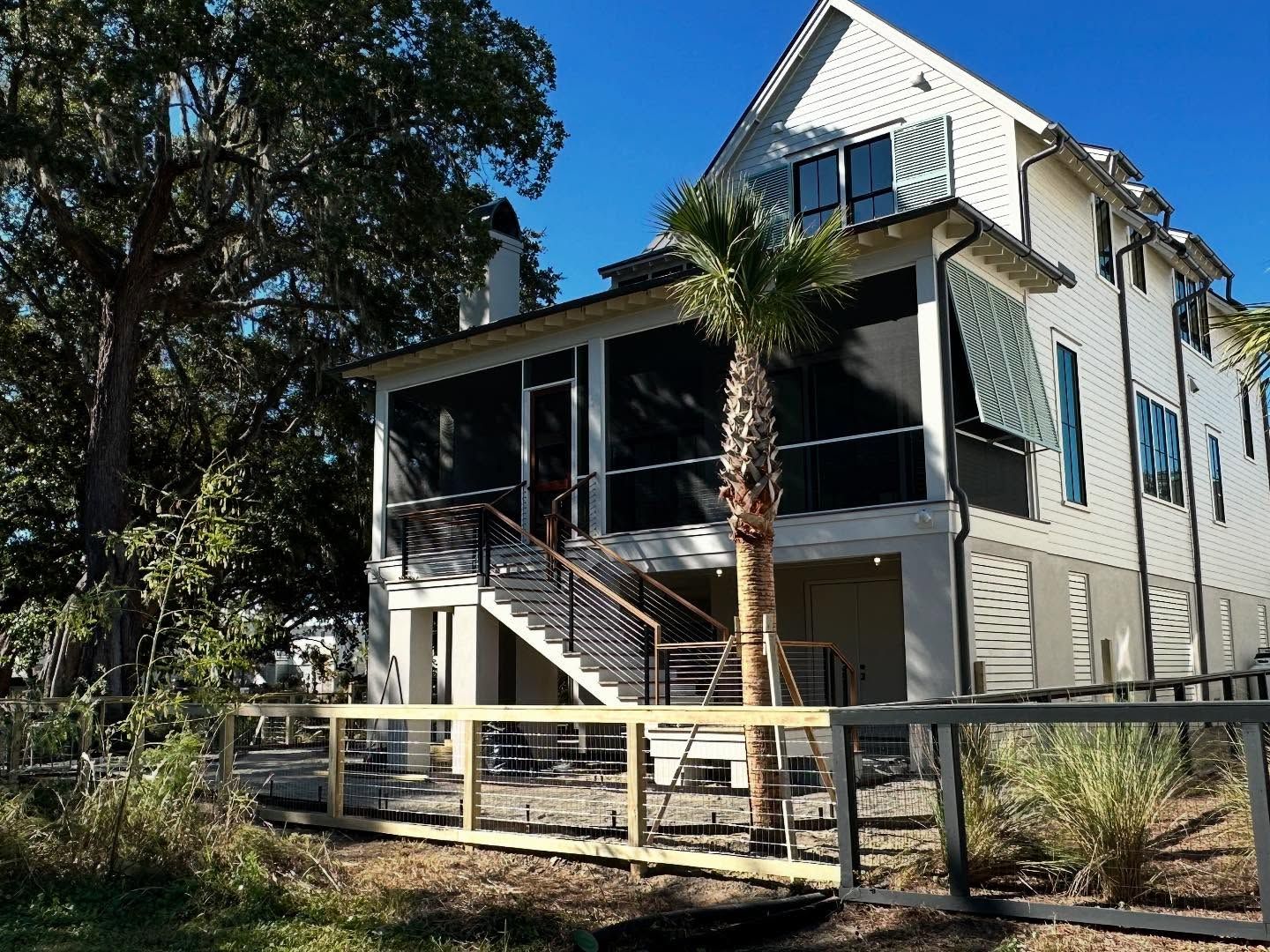 Two-story white house with a screened porch, front stairs, and a fenced yard under trees