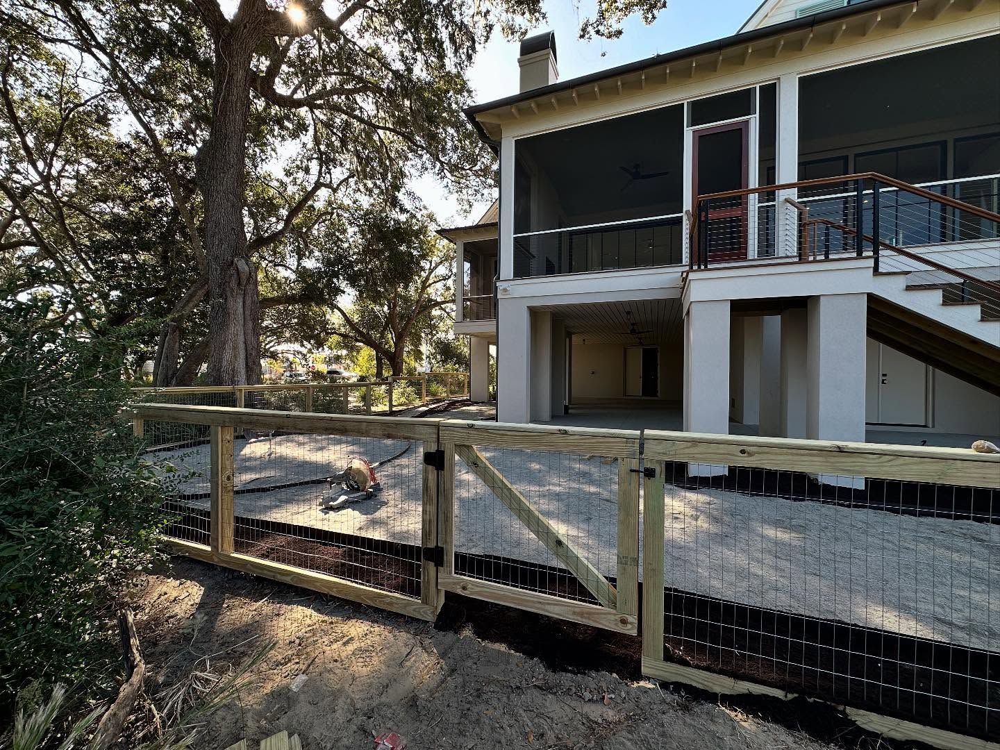 House with raised deck and stairs behind a chain-link fence in a wooded yard