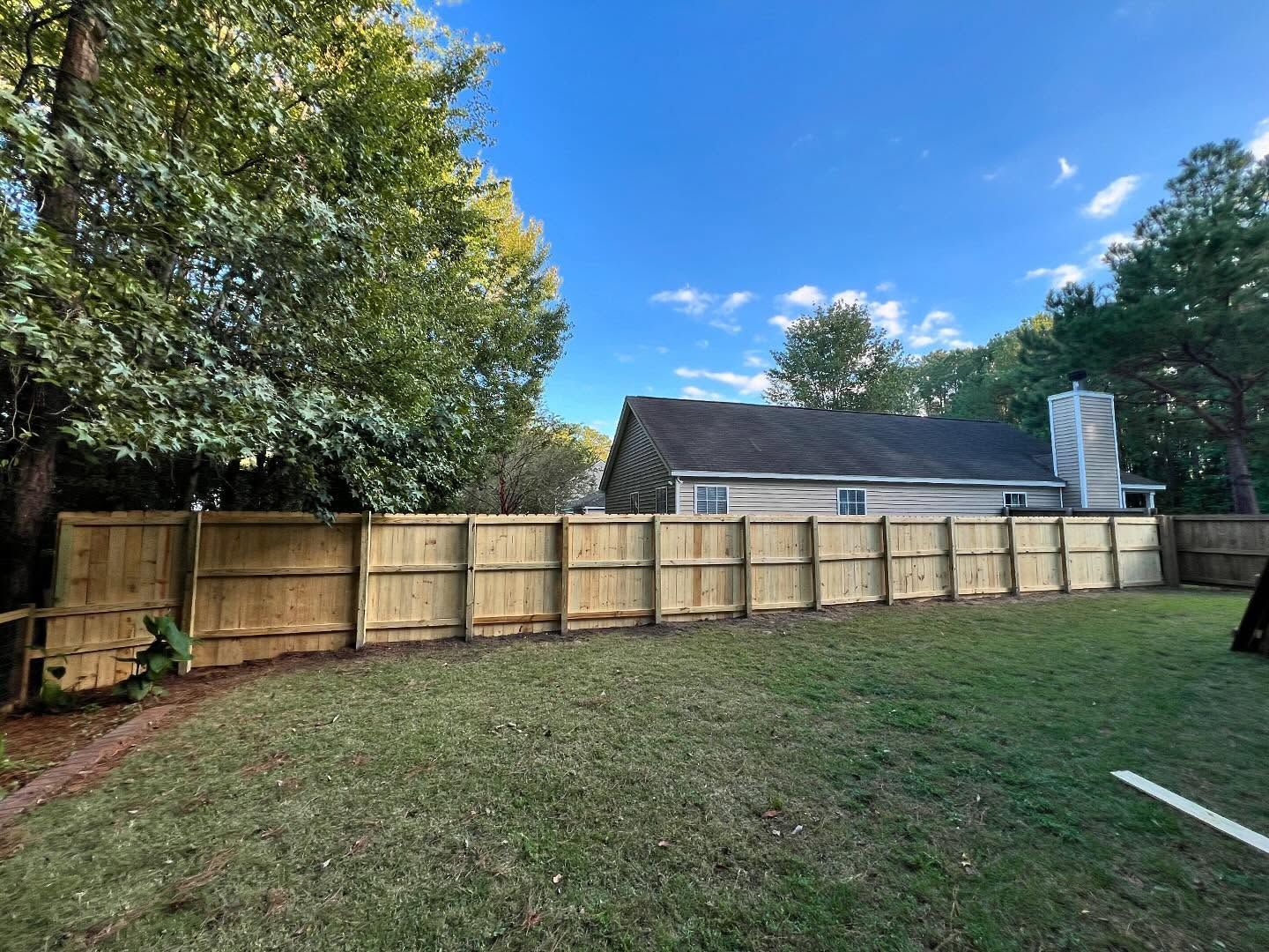 Backyard with newly built wooden fence, green lawn, and trees under a blue sky