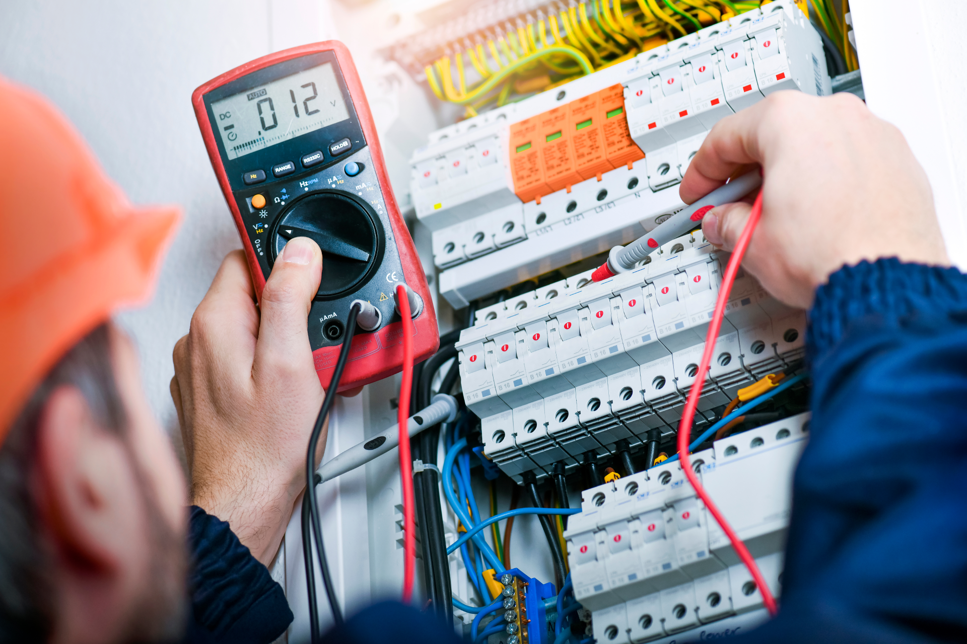 Technician testing electrical panel with a multimeter and red probe wires