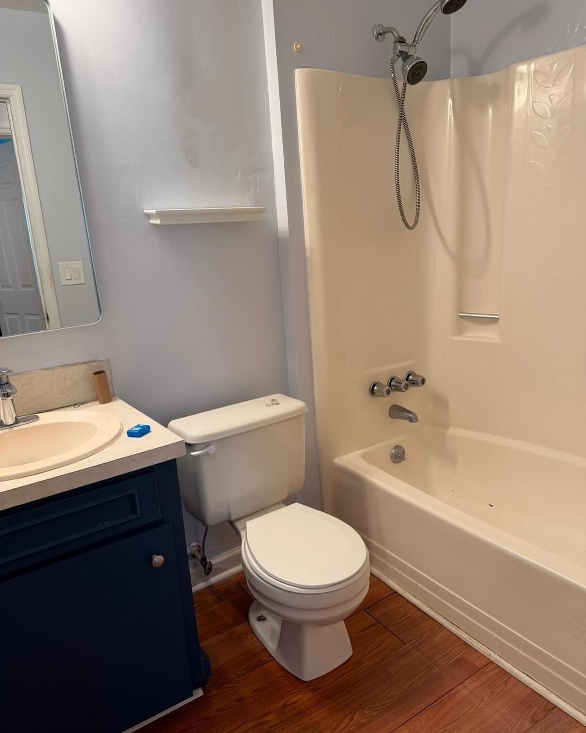 Small bathroom with toilet, sink vanity, and beige shower-tub surround on wood-look floor.