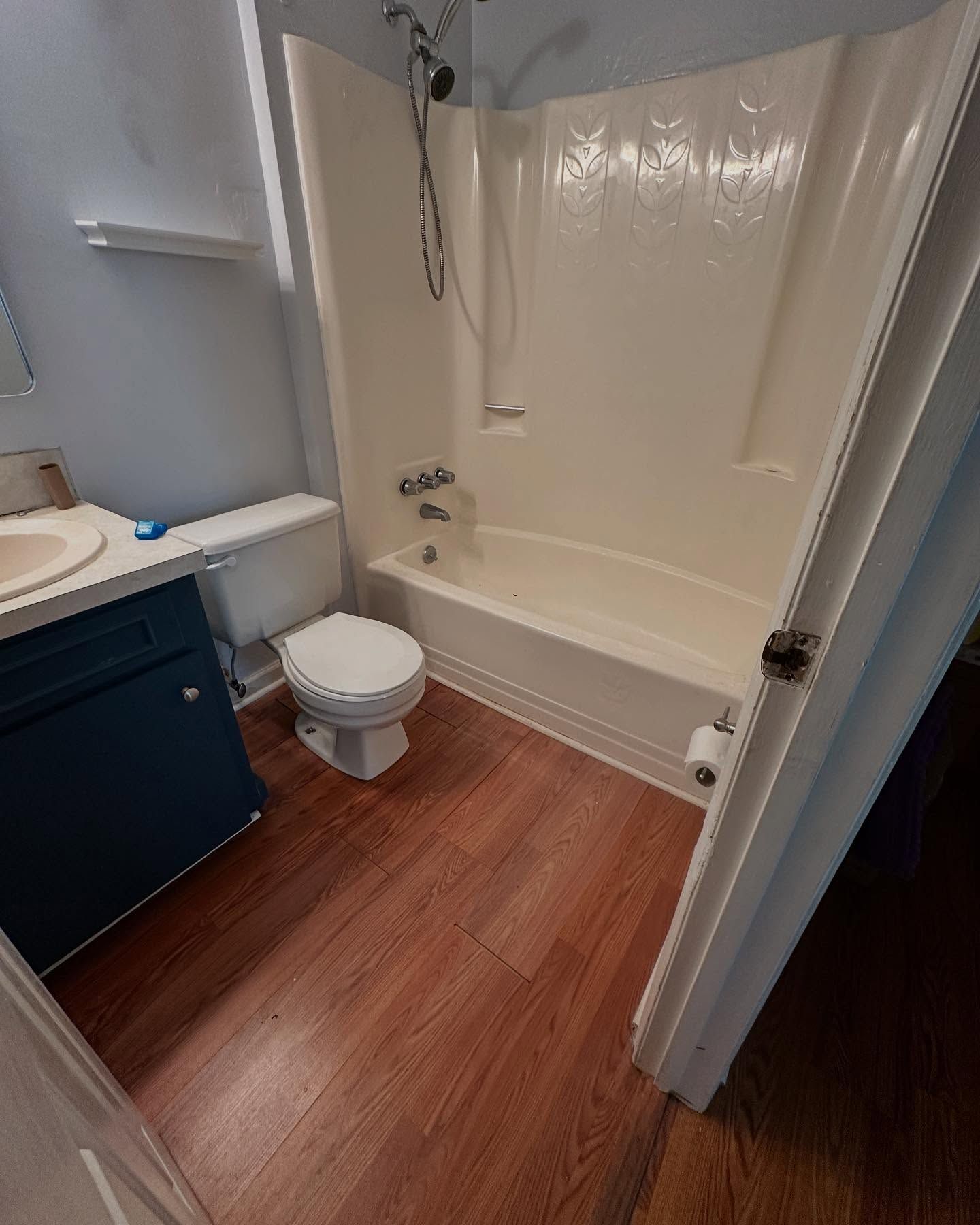 Small bathroom with white tub-shower, toilet, dark vanity, and wood-look floor.