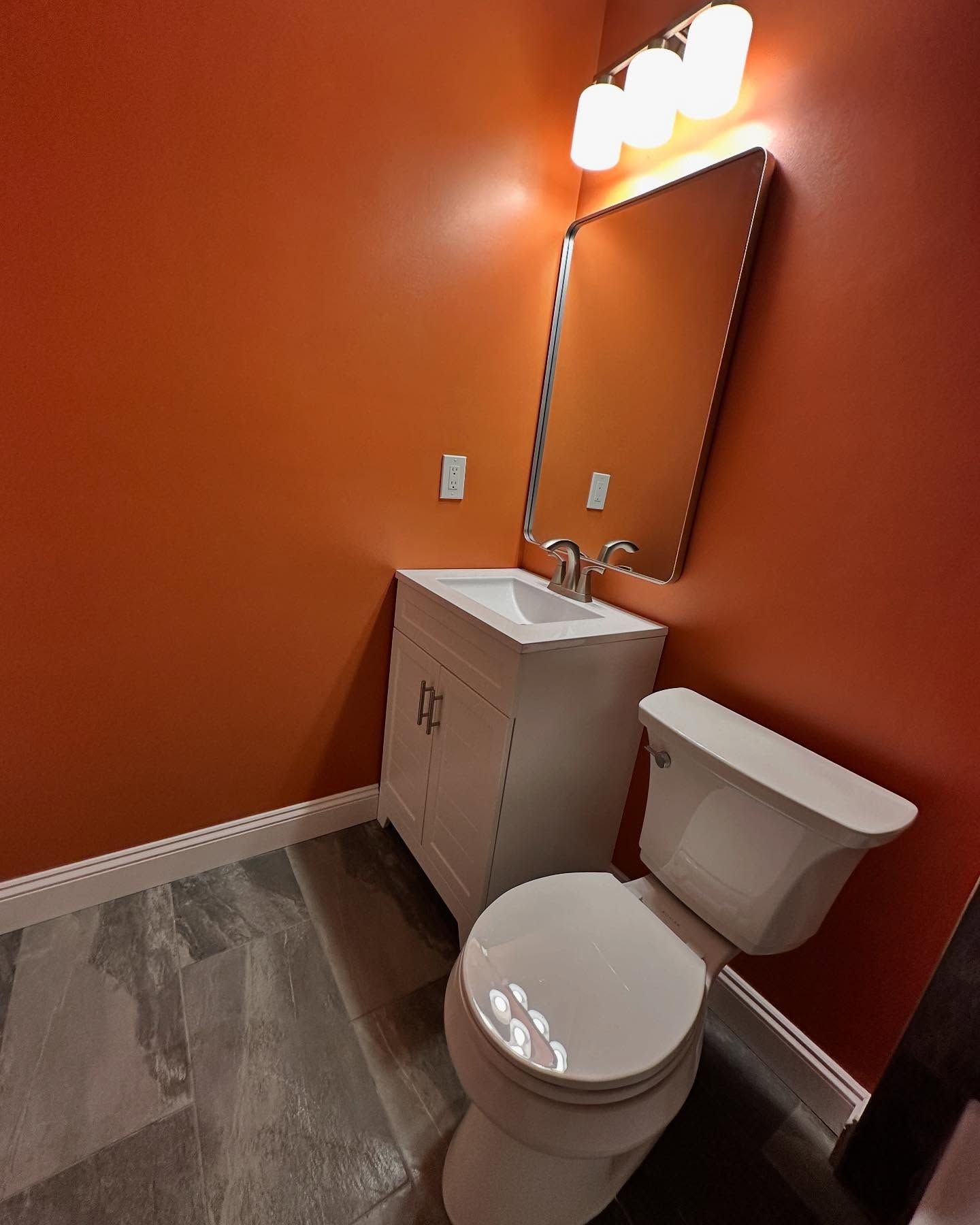 Small bathroom with orange walls, white vanity, mirror, and toilet.