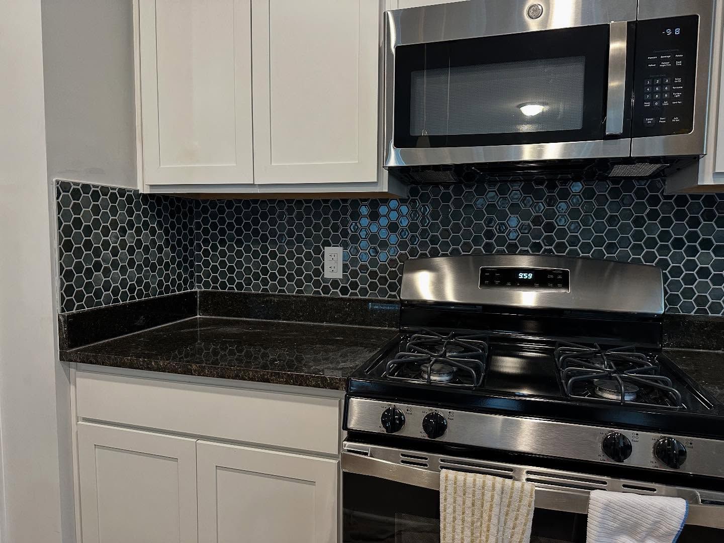 Modern kitchen with white cabinets, black countertop, blue tile backsplash, and stainless steel stove and microwave