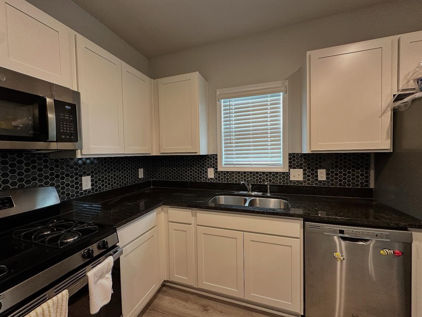 Small kitchen with white cabinets, black countertops, stainless appliances, and a window above the sink.