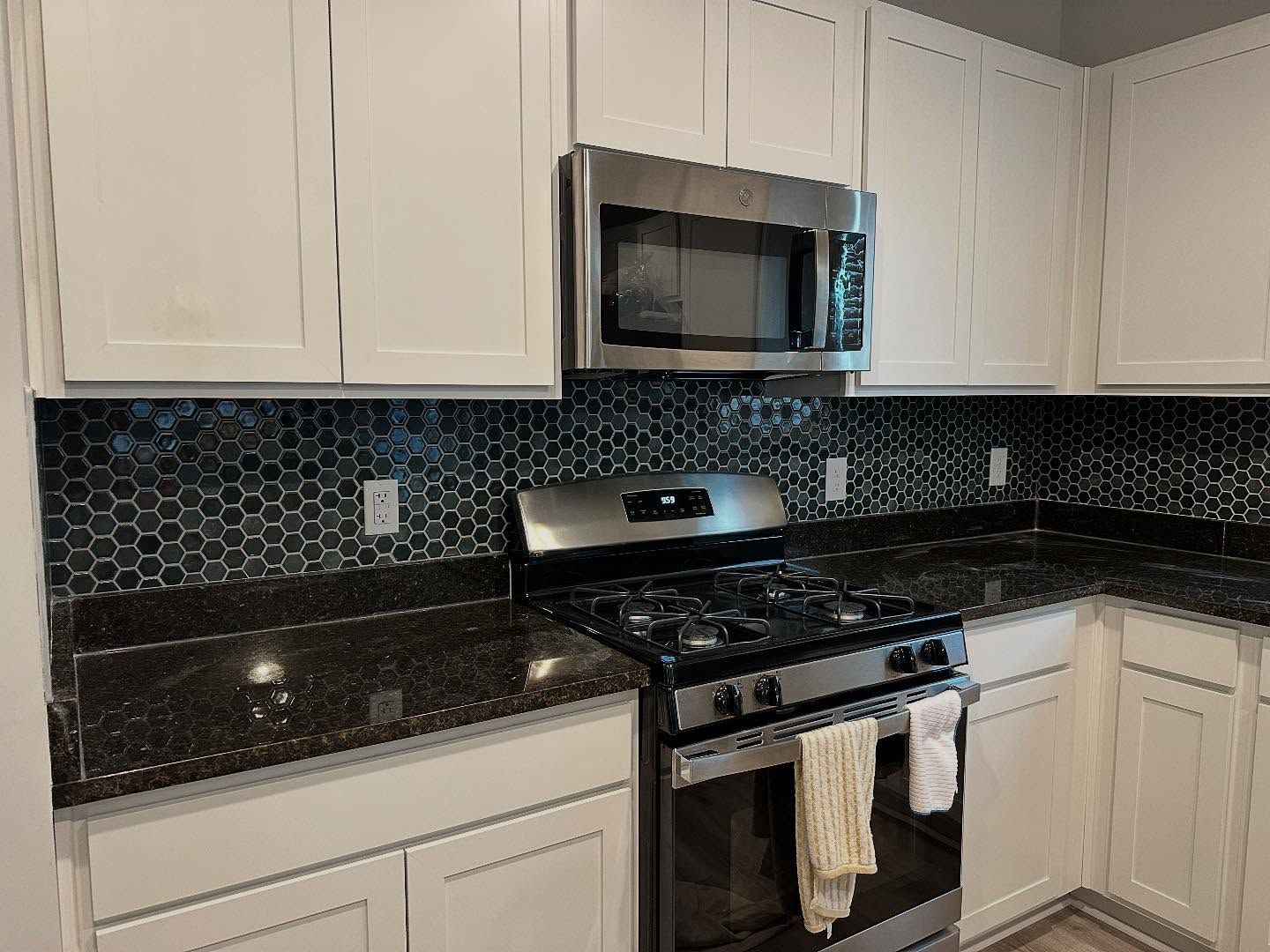Modern kitchen with white cabinets, black granite counters, black tile backsplash, and stainless steel appliances