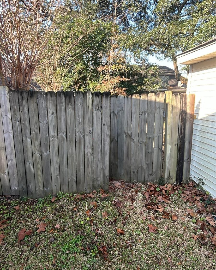 Weathered wooden fence beside a white house, with fallen leaves and grass in a backyard