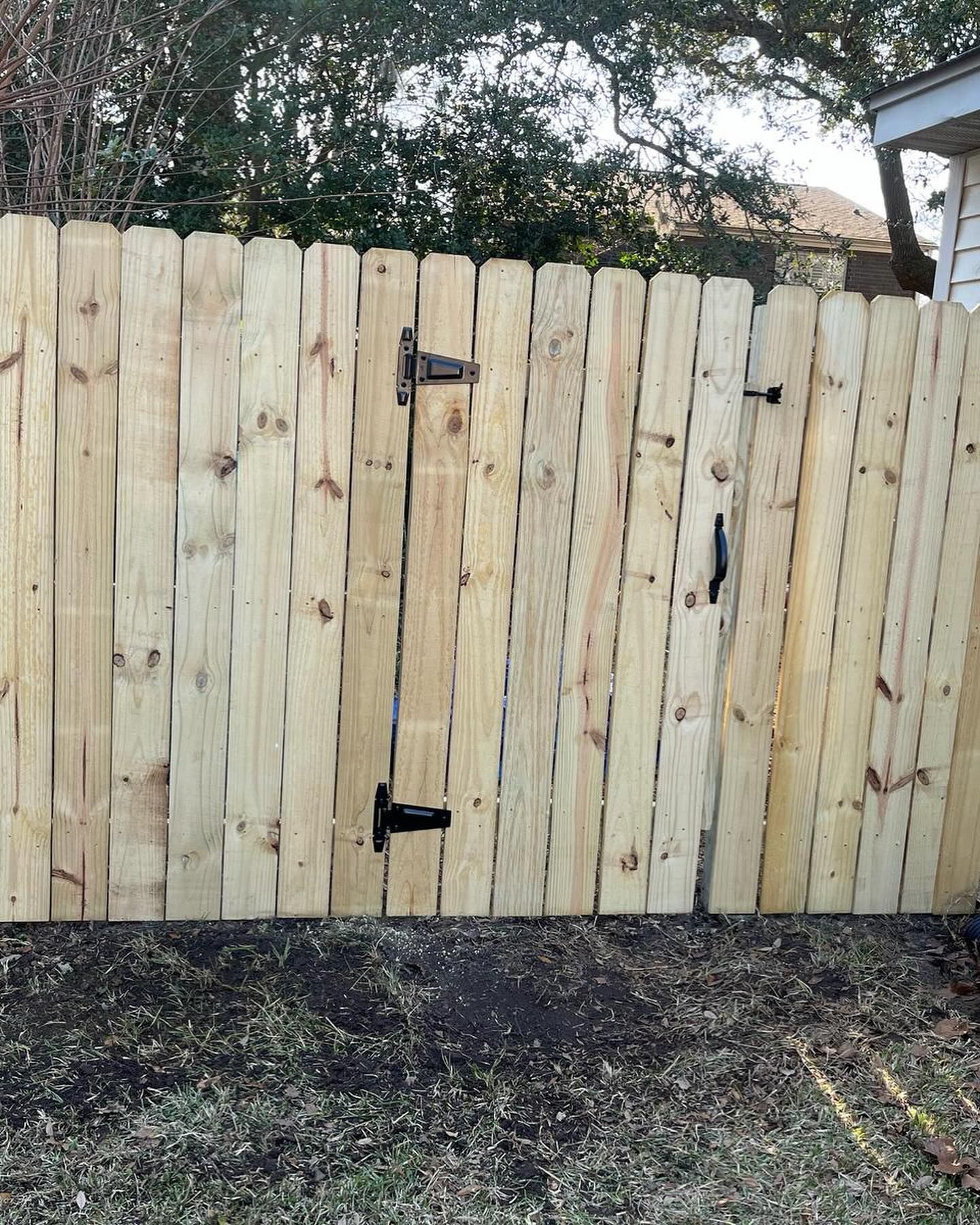 New wooden fence with black hinges and latch in a yard