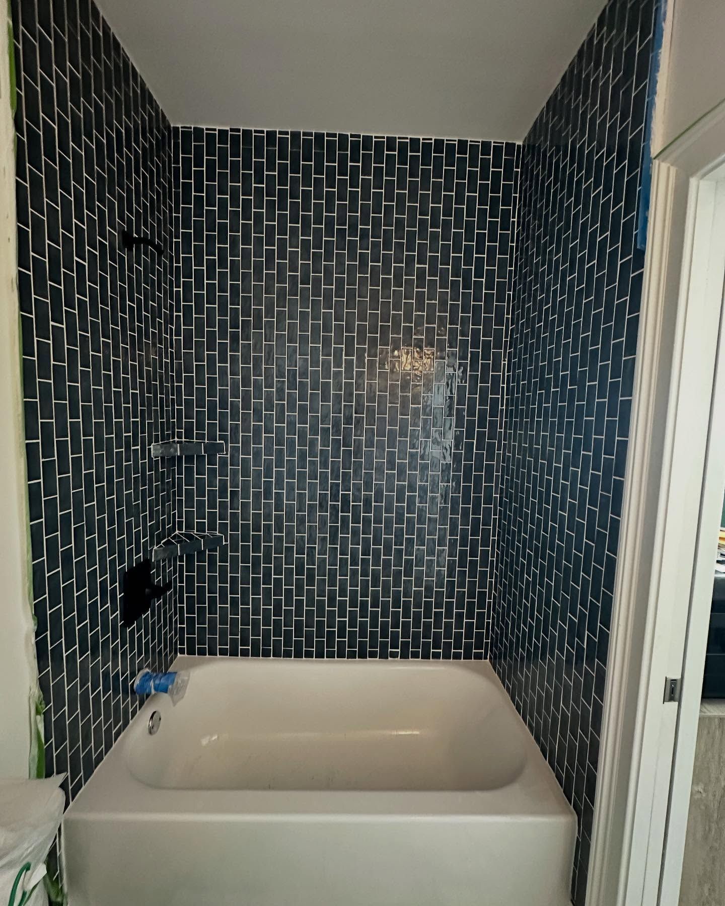 Bathroom with a white bathtub and dark patterned tile walls, viewed from the doorway.