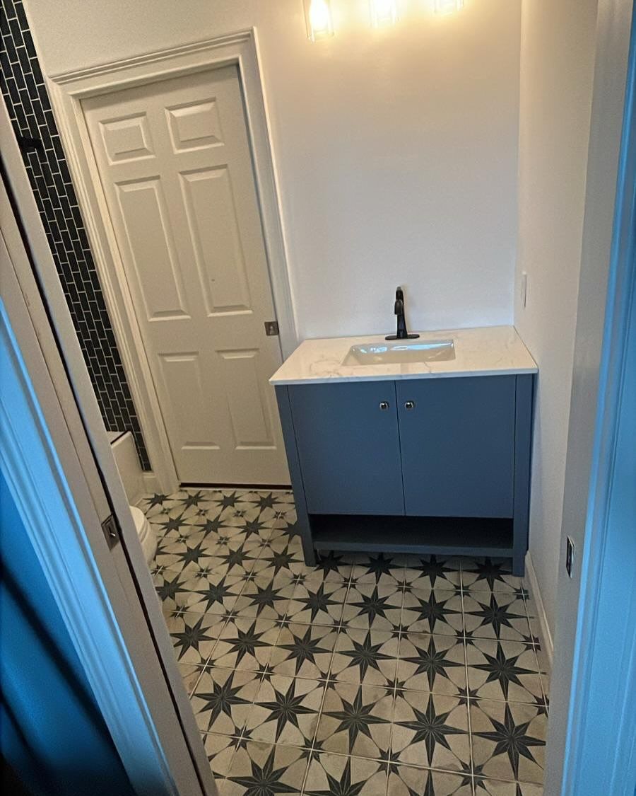 Small bathroom with patterned tile floor, blue vanity, sink, and white door.