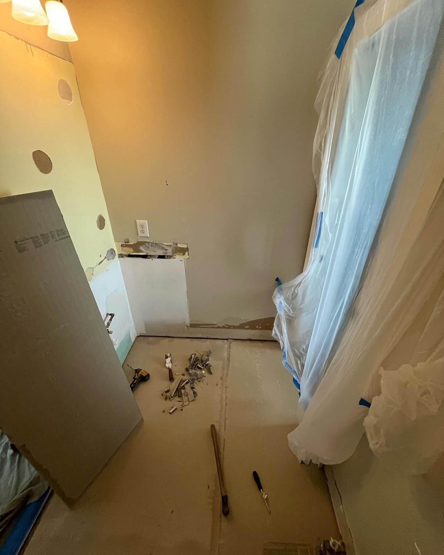 Small room under renovation with tools and debris on the floor, a blue-covered window, and a white sink at the back.