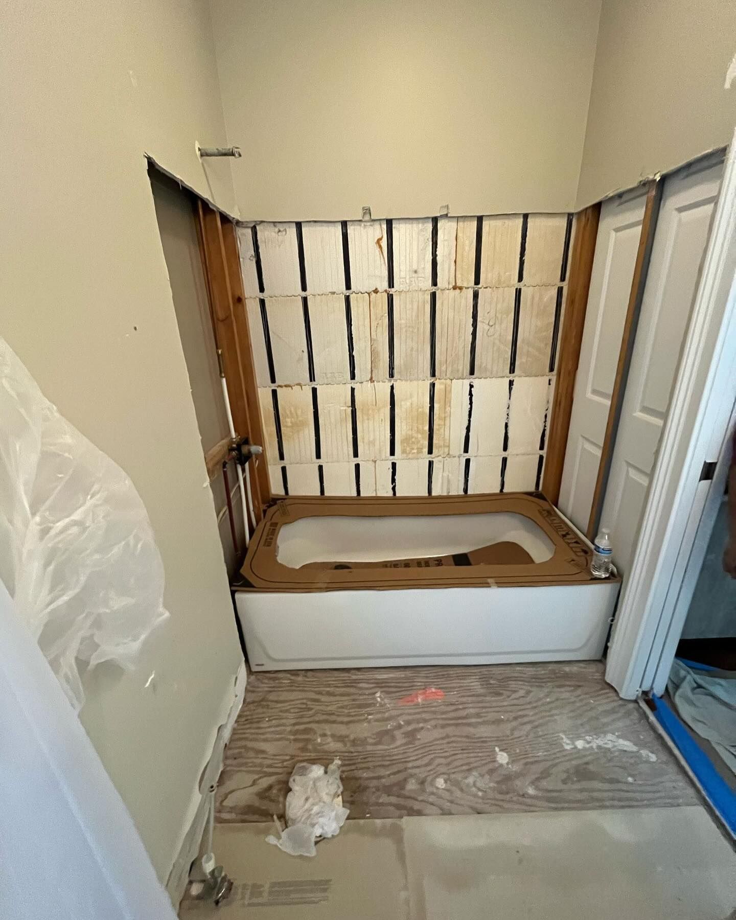 Unfinished bathroom with a built-in tub, exposed wall insulation, and protective floor covering during renovation
