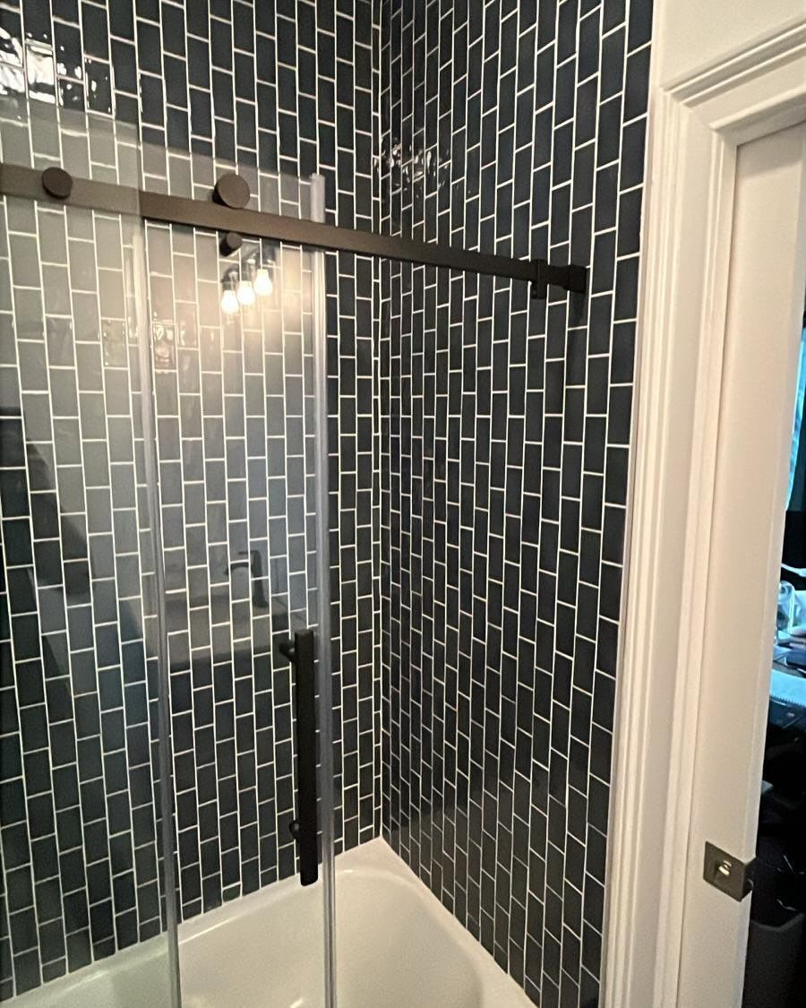 Tiled shower stall with dark mosaic walls, glass door, and white shower base