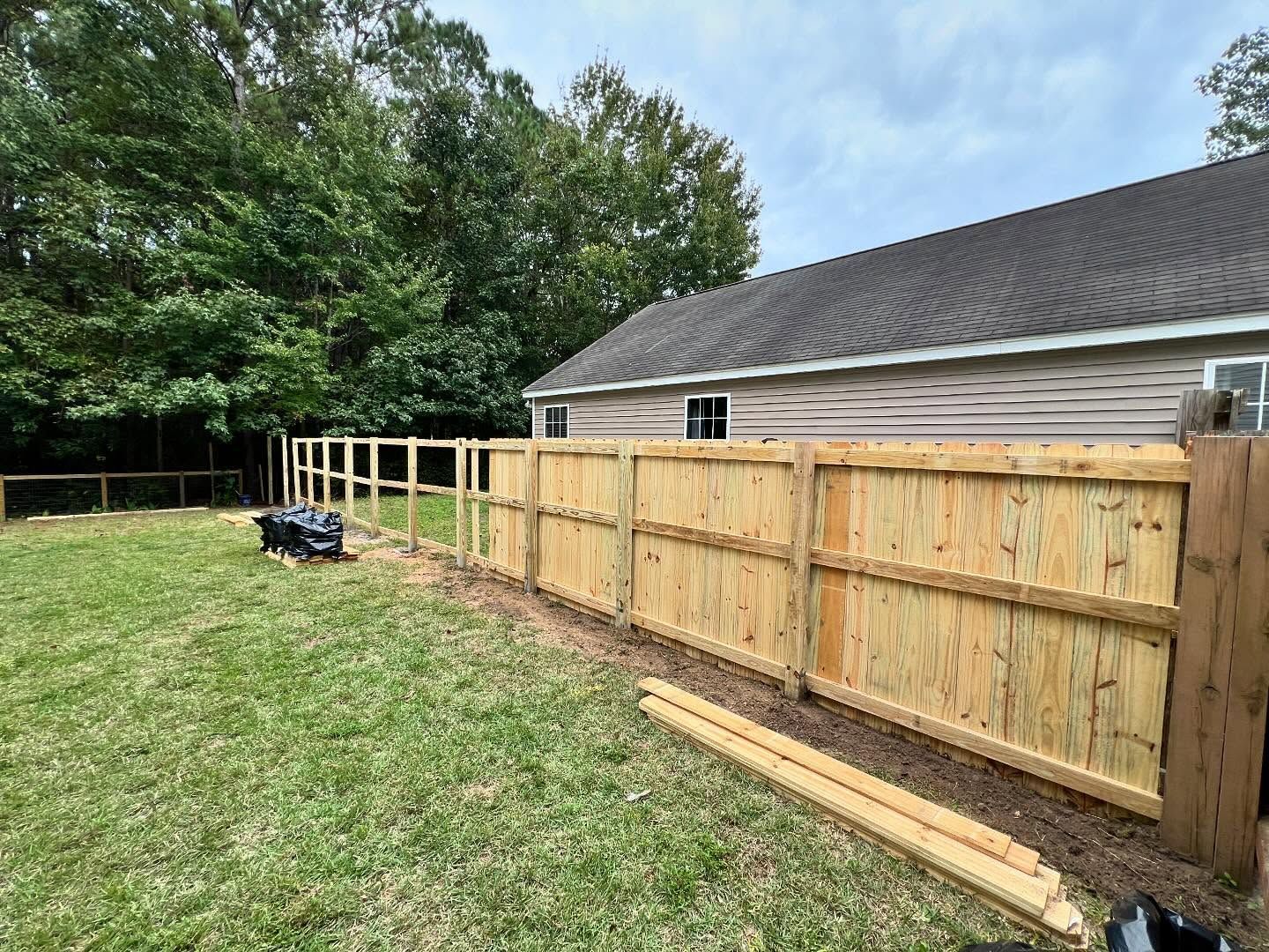 Wooden privacy fence beside a house in a grassy backyard, with a power tool on the lawn.