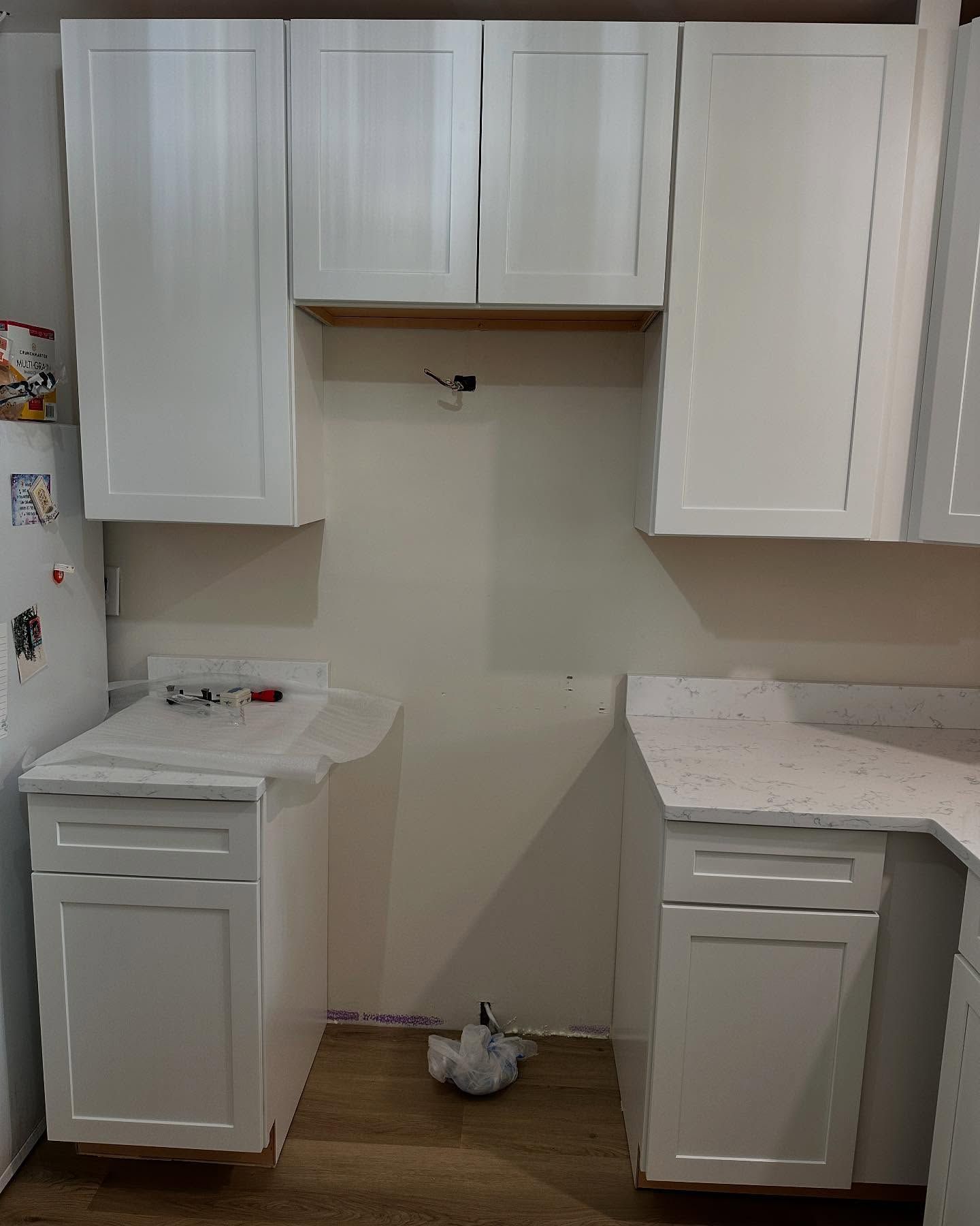 White kitchen cabinets and countertops around an unfinished wall opening.