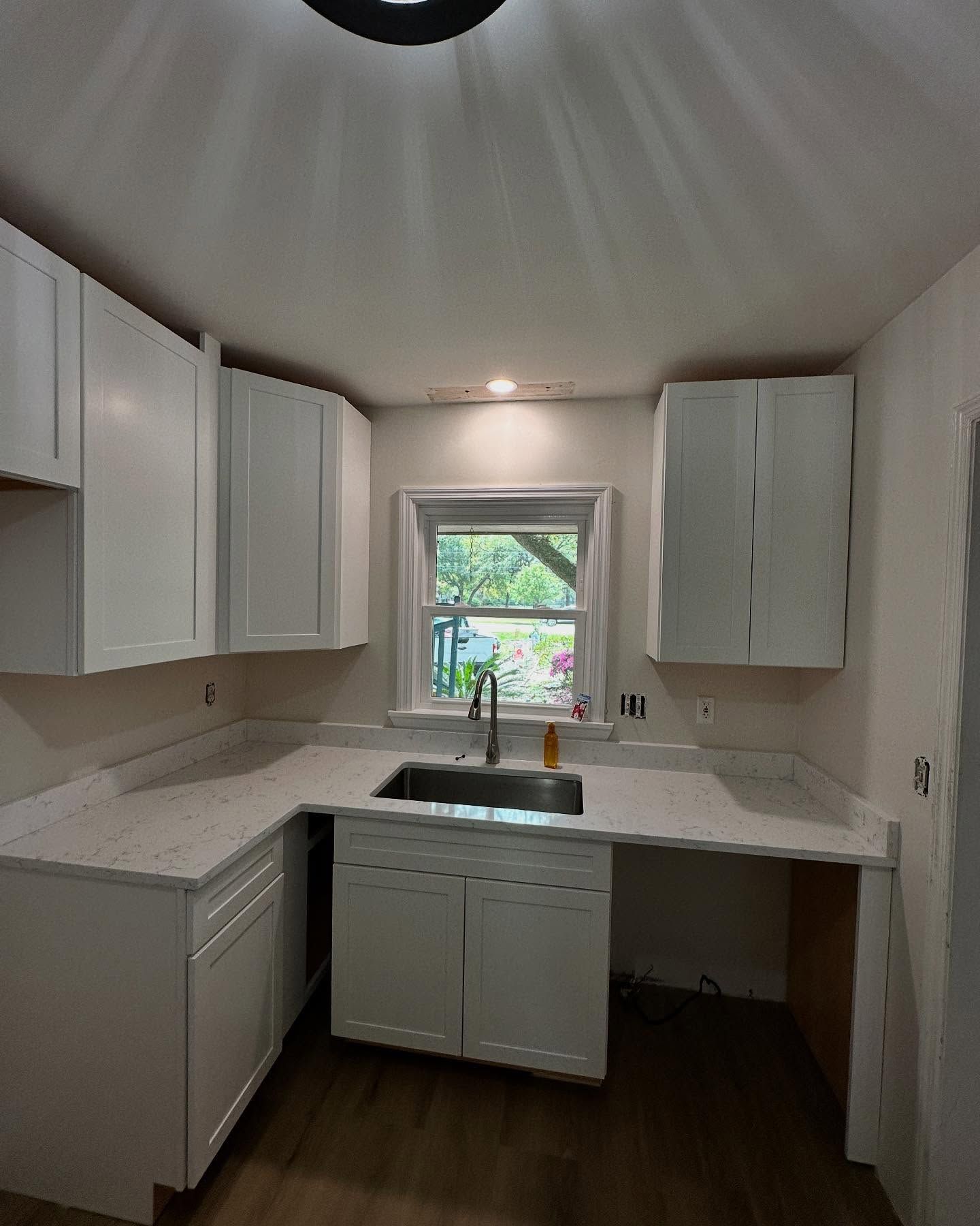 Small white kitchen with L-shaped counters, window over sink, and dark wood floor.