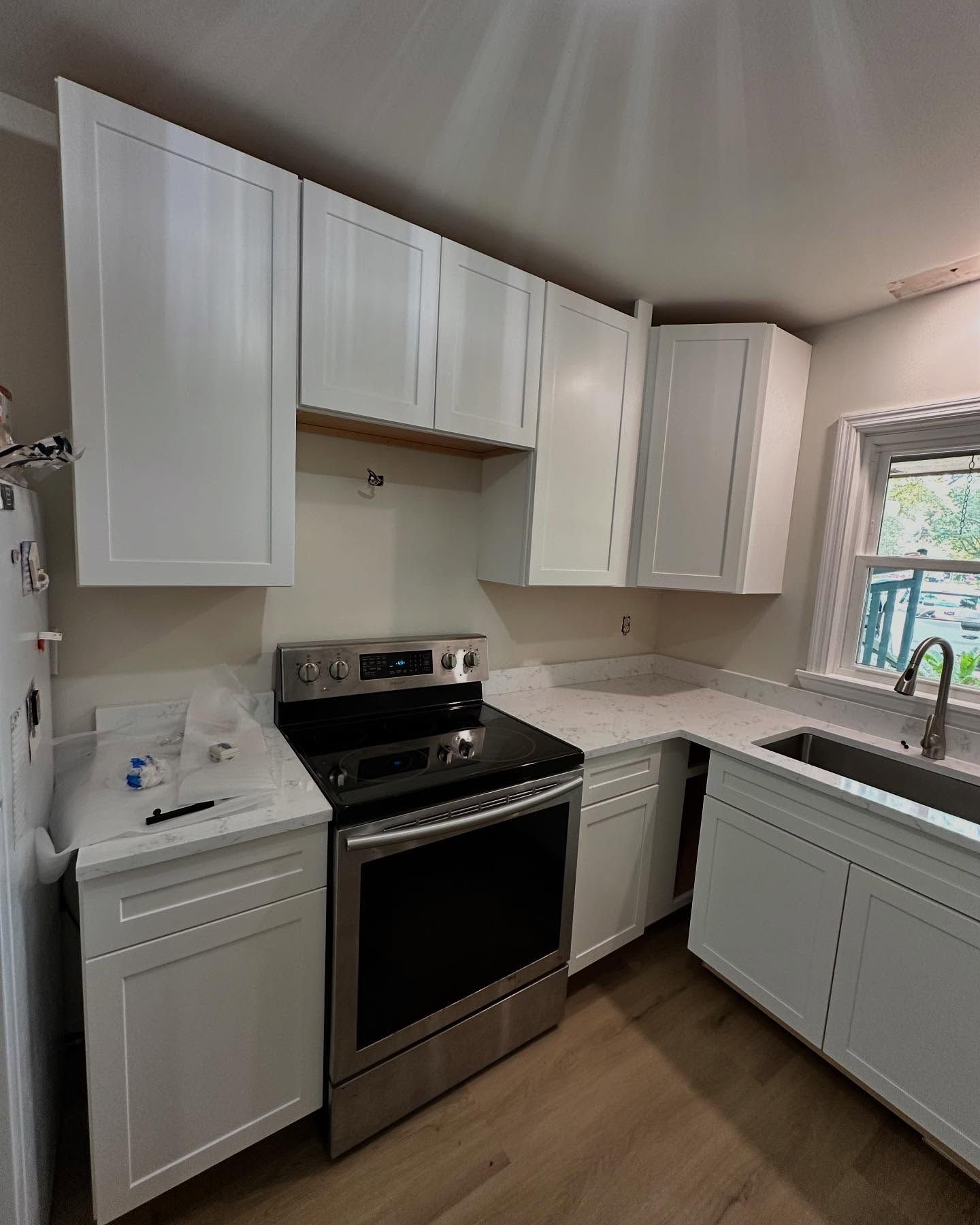 Modern white kitchen with stainless steel stove, white cabinets, and a window over the sink