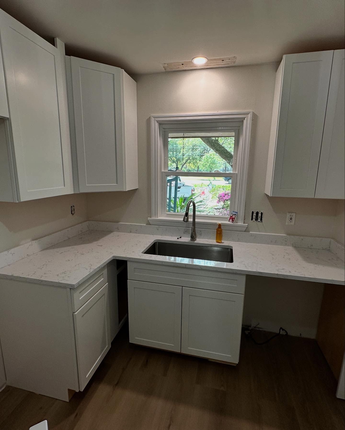 Bright kitchen with white cabinets, light countertops, and a sink under a window.