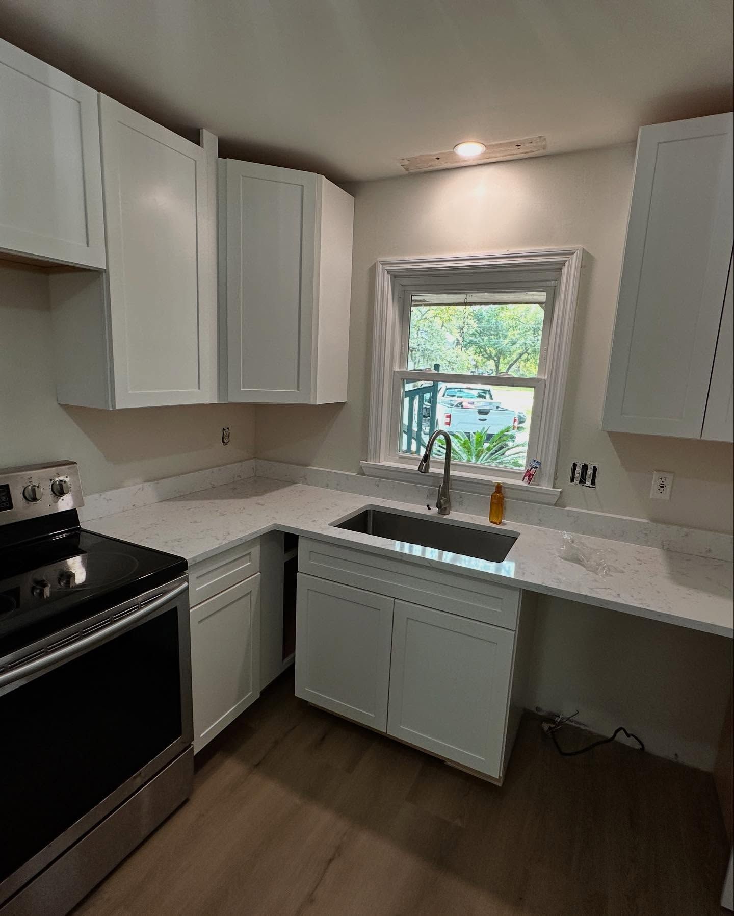 Small white kitchen with cabinets, black stove, and sink under a window.