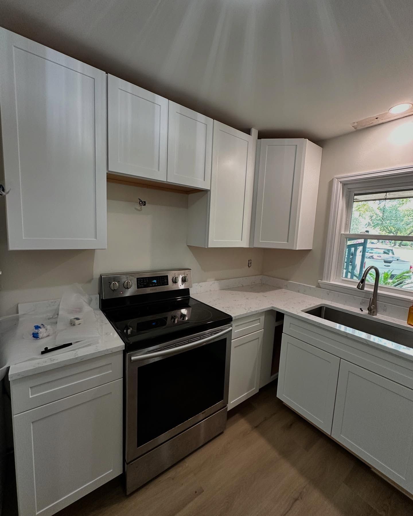 Modern kitchen with white cabinets, stainless steel stove, and sink under a window.