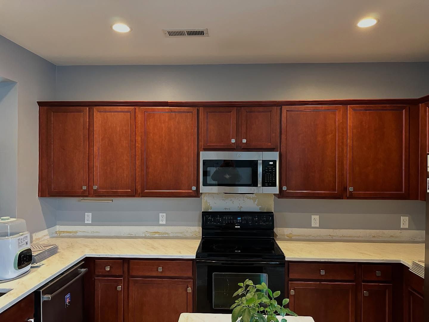 Kitchen with wooden cabinets, black stove and microwave, and light countertops under recessed ceiling lights