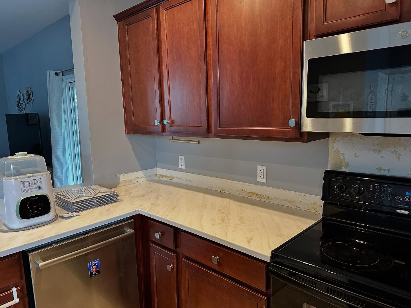 Kitchen with wooden cabinets, light countertops, black stove, and stainless steel microwave.