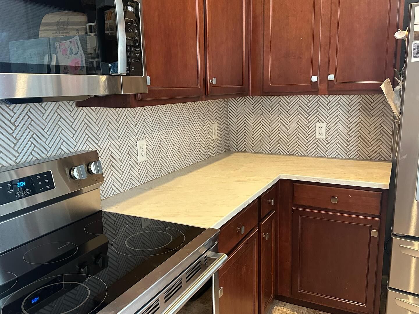 Kitchen corner with dark wood cabinets, stainless stove, and light countertop against a patterned backsplash