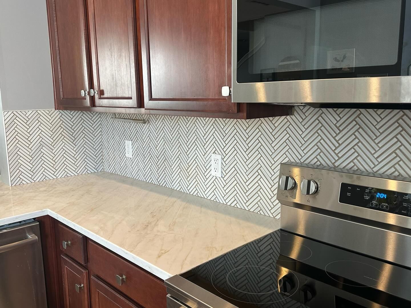 Modern kitchen with dark cabinets, light wood countertop, patterned backsplash, and stainless steel stove and microwave