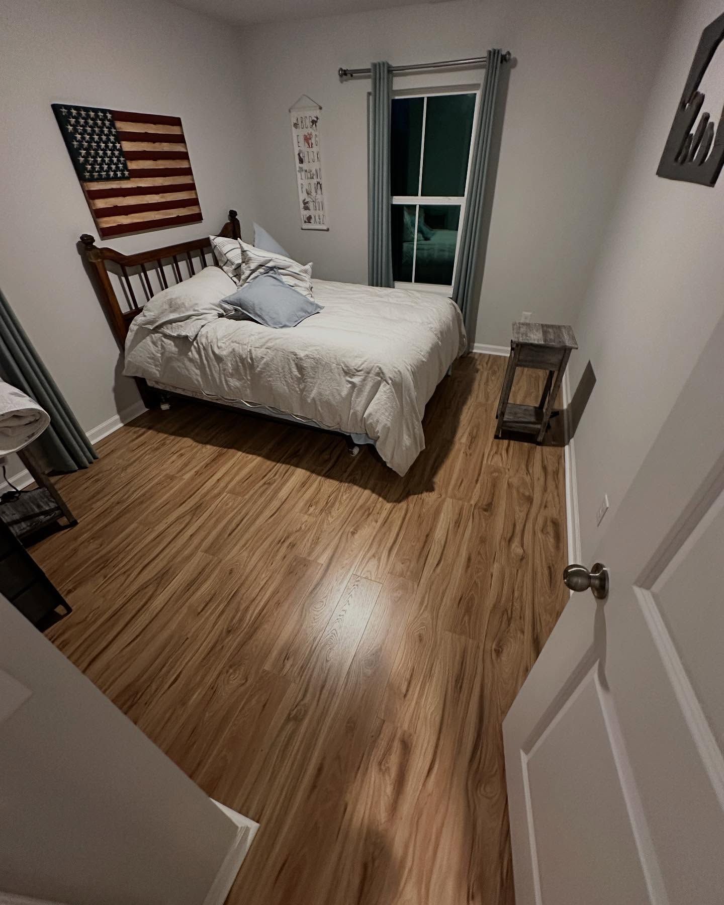 Small bedroom with a bed, wood floor, American flag wall art, and a balcony door.