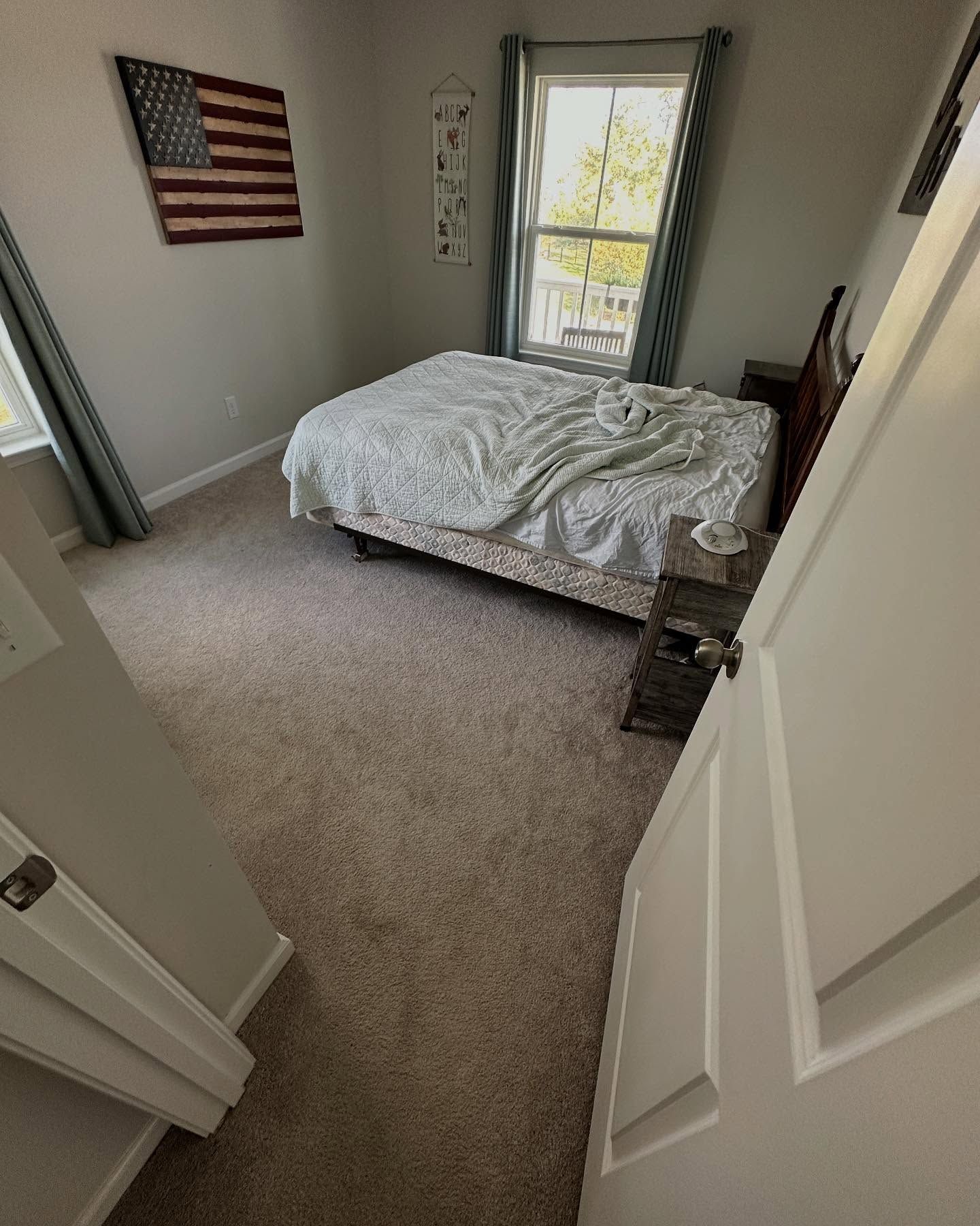 Small bedroom with unmade bed, window, and American flag wall art.