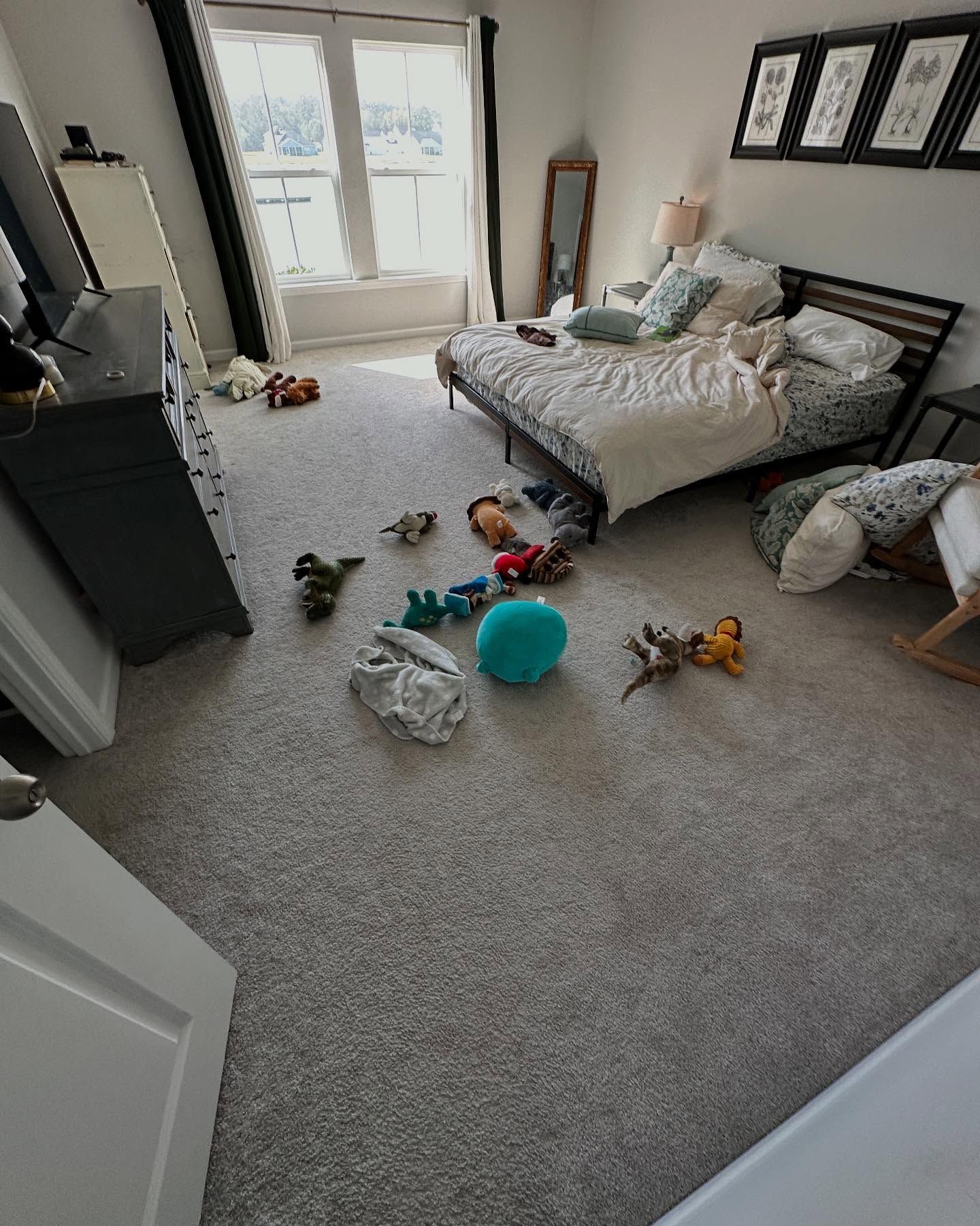 Messy bedroom with an unmade bed, toys scattered on carpet, and daylight through a window.