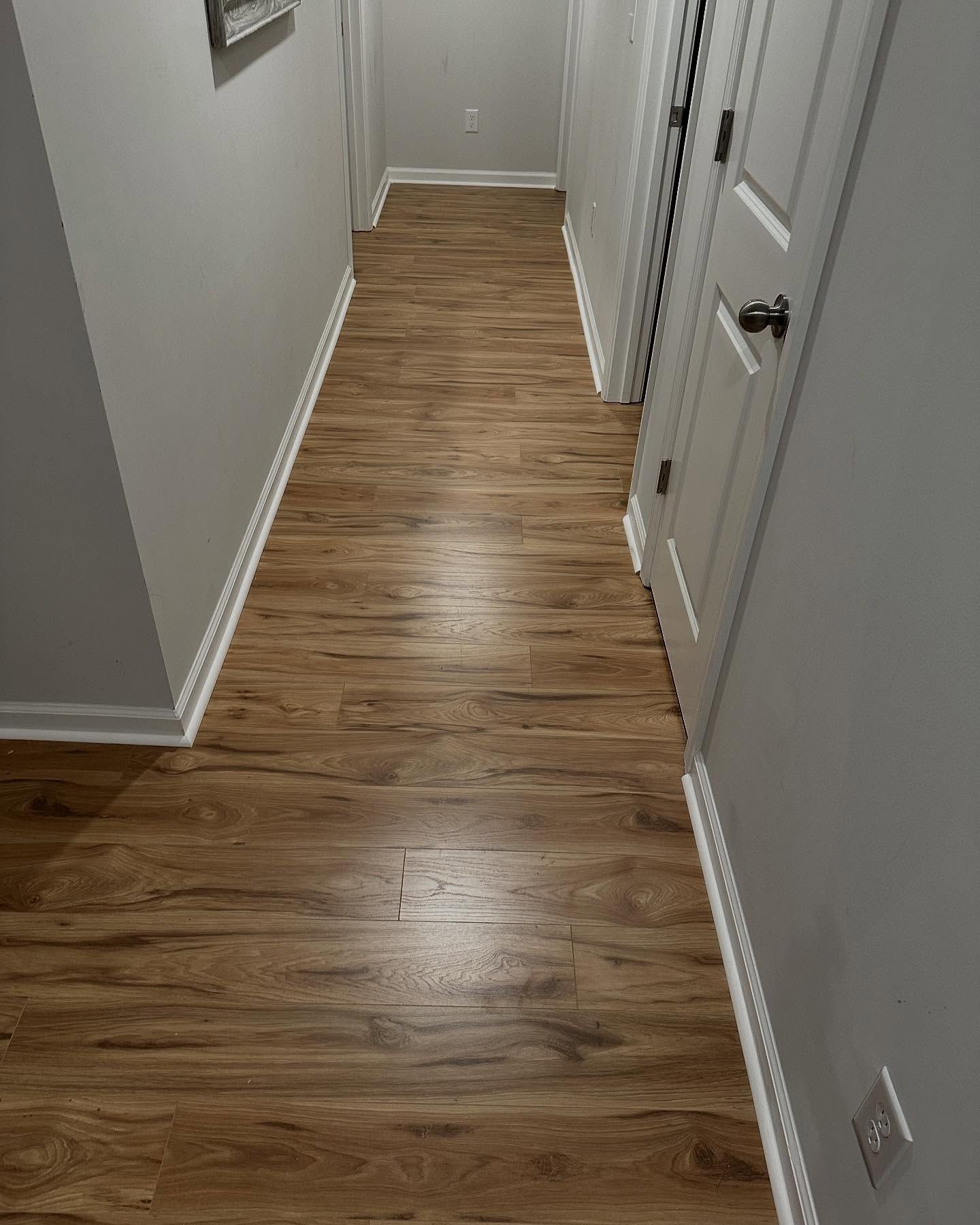 Narrow hallway with wood-look flooring, white doors, and gray walls.