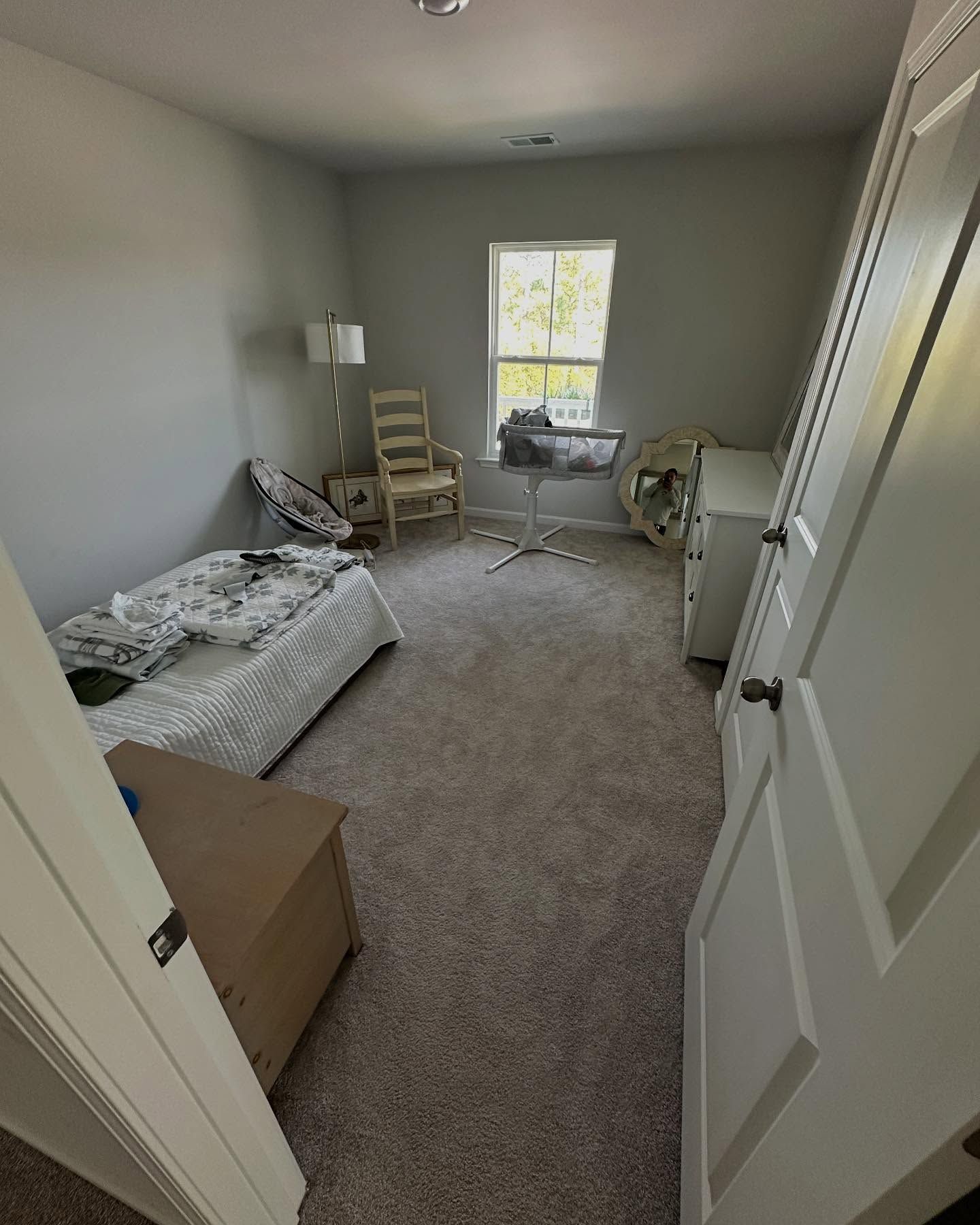 Small bedroom with unmade bed, chair, desk, lamp, and window, viewed through an open door